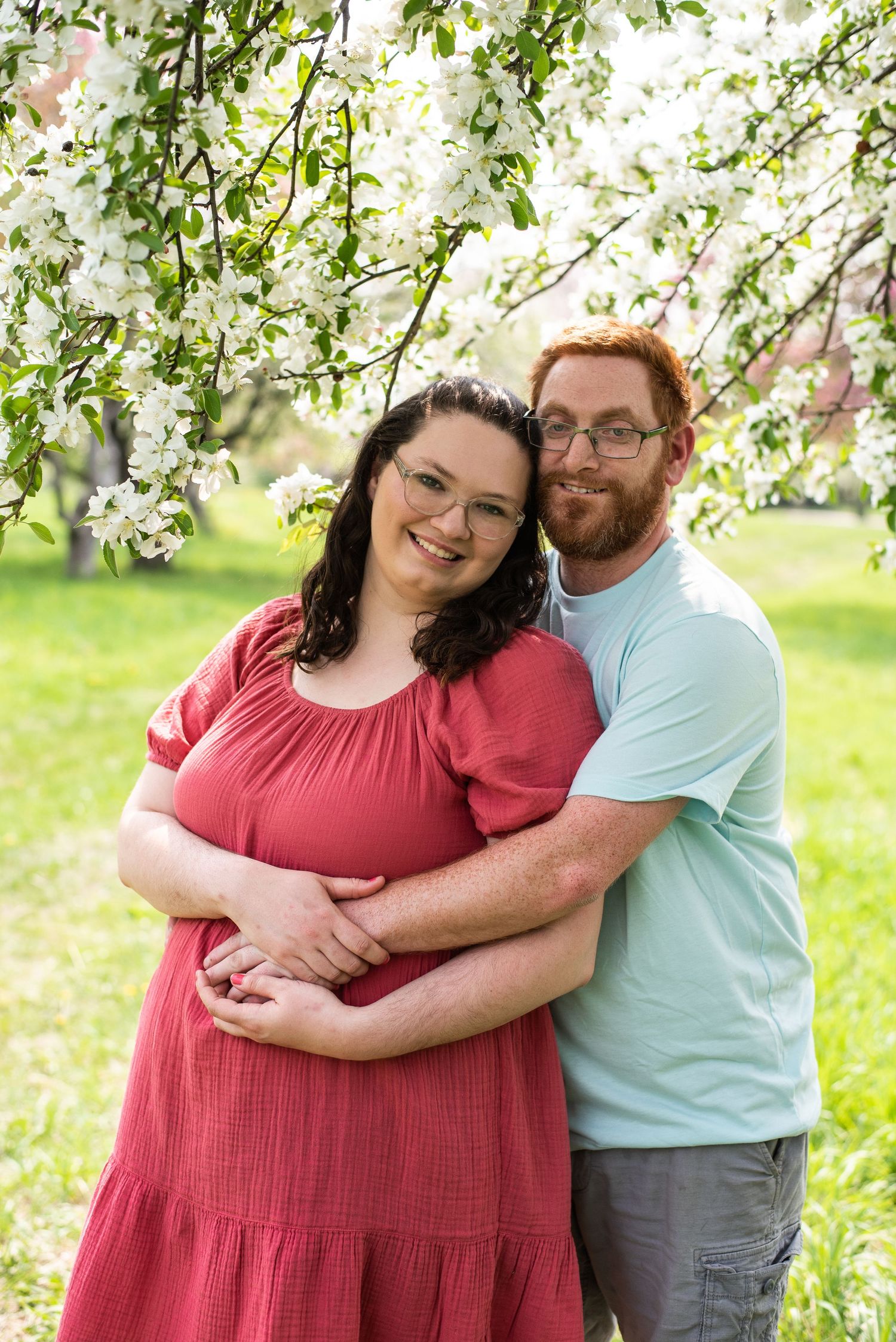 A couple embraces under blooming spring cherry blossoms in a sunny garden.