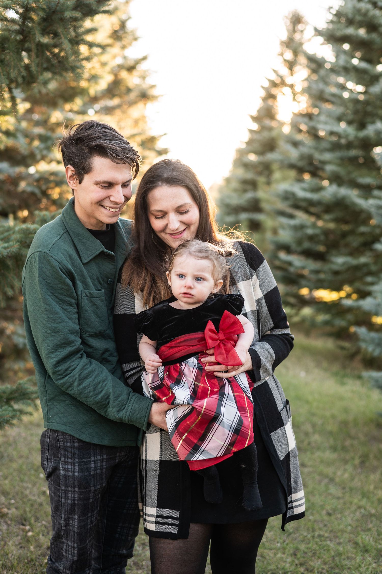 A family stands together among evergreen trees at sunset in winter clothing.