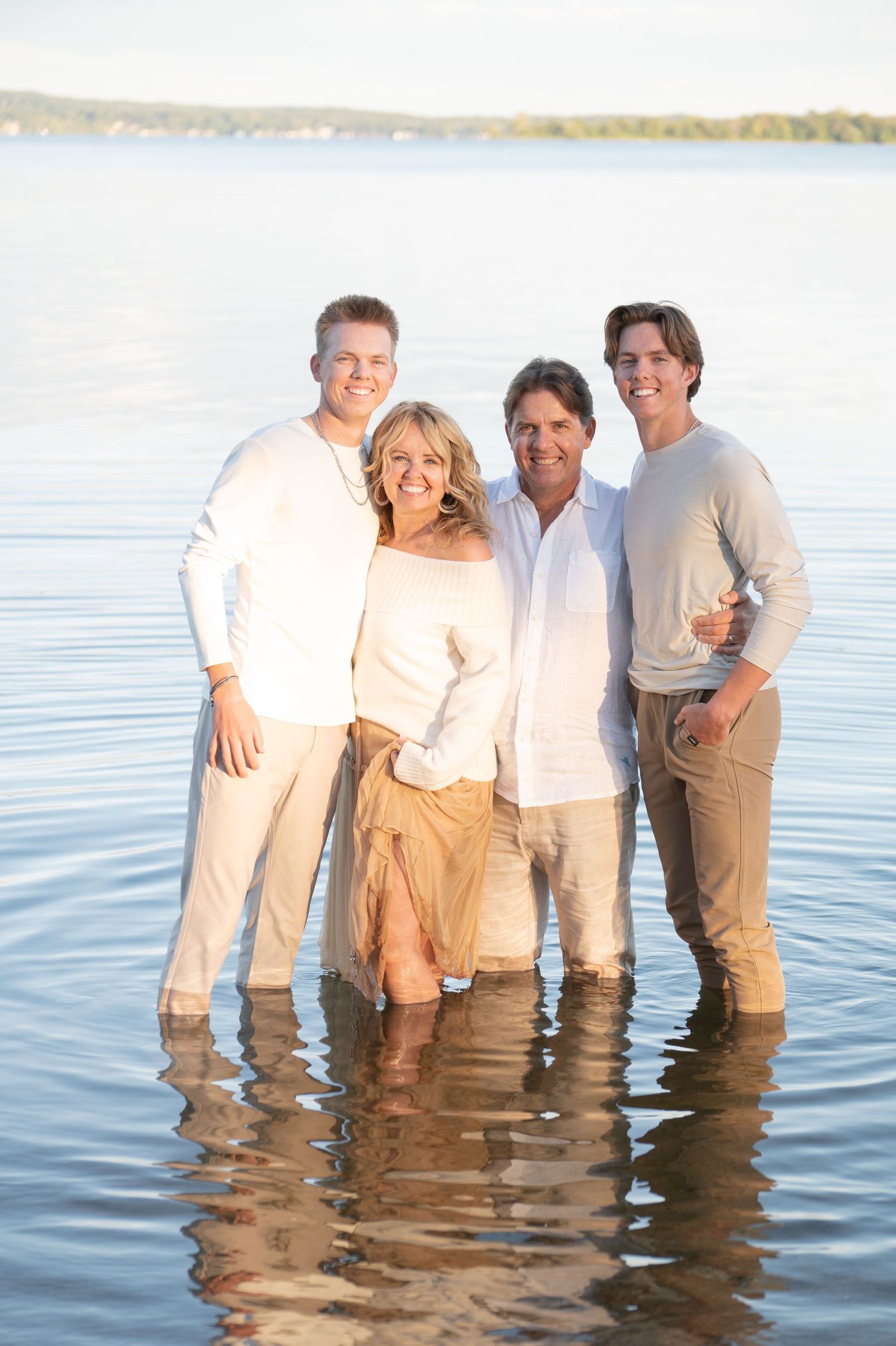 A family of four poses together while standing in shallow water at sunset.