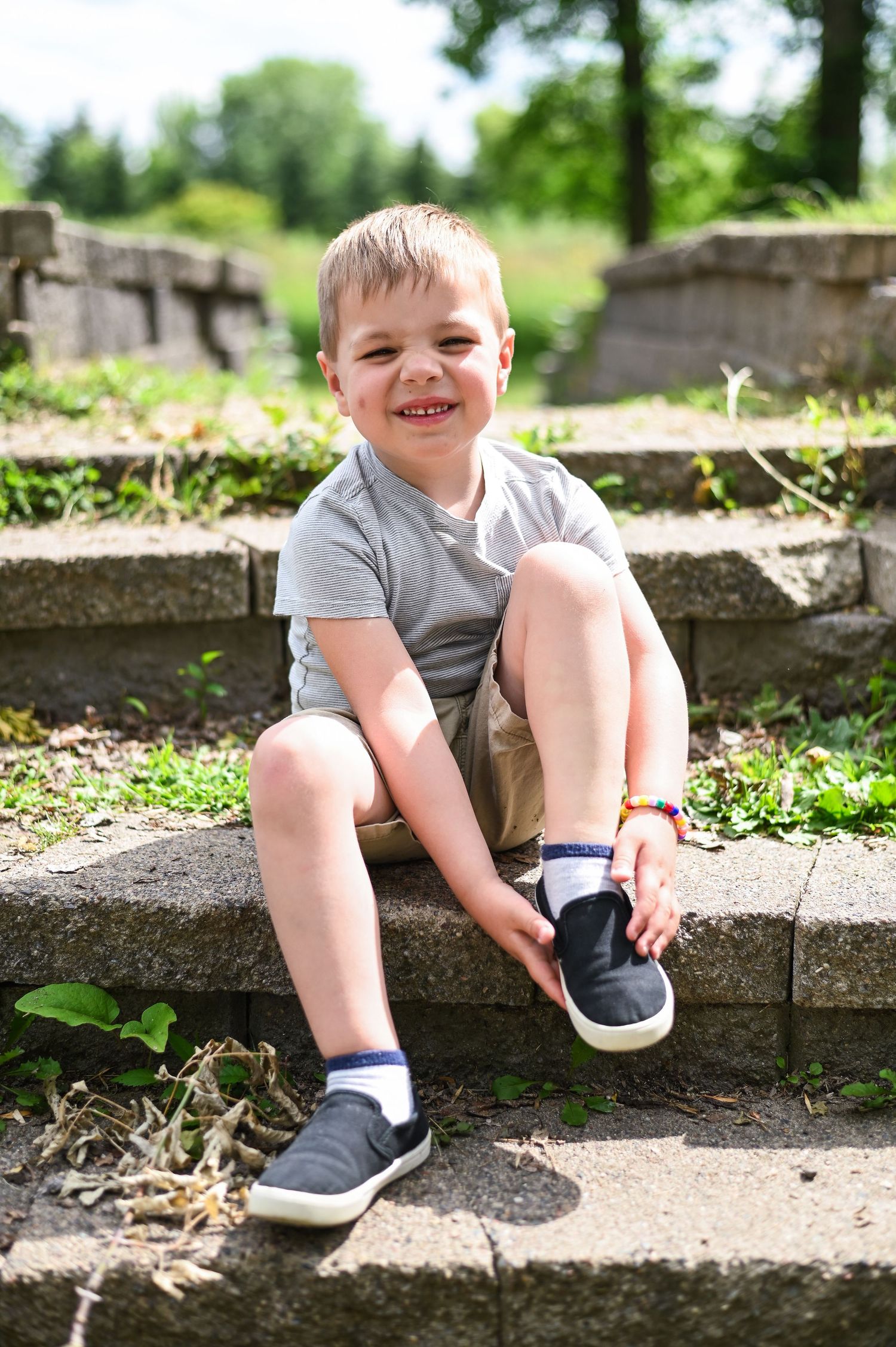 Close up view of small feet in navy blue shoes sitting on stone steps in a sunny outdoor setting.
