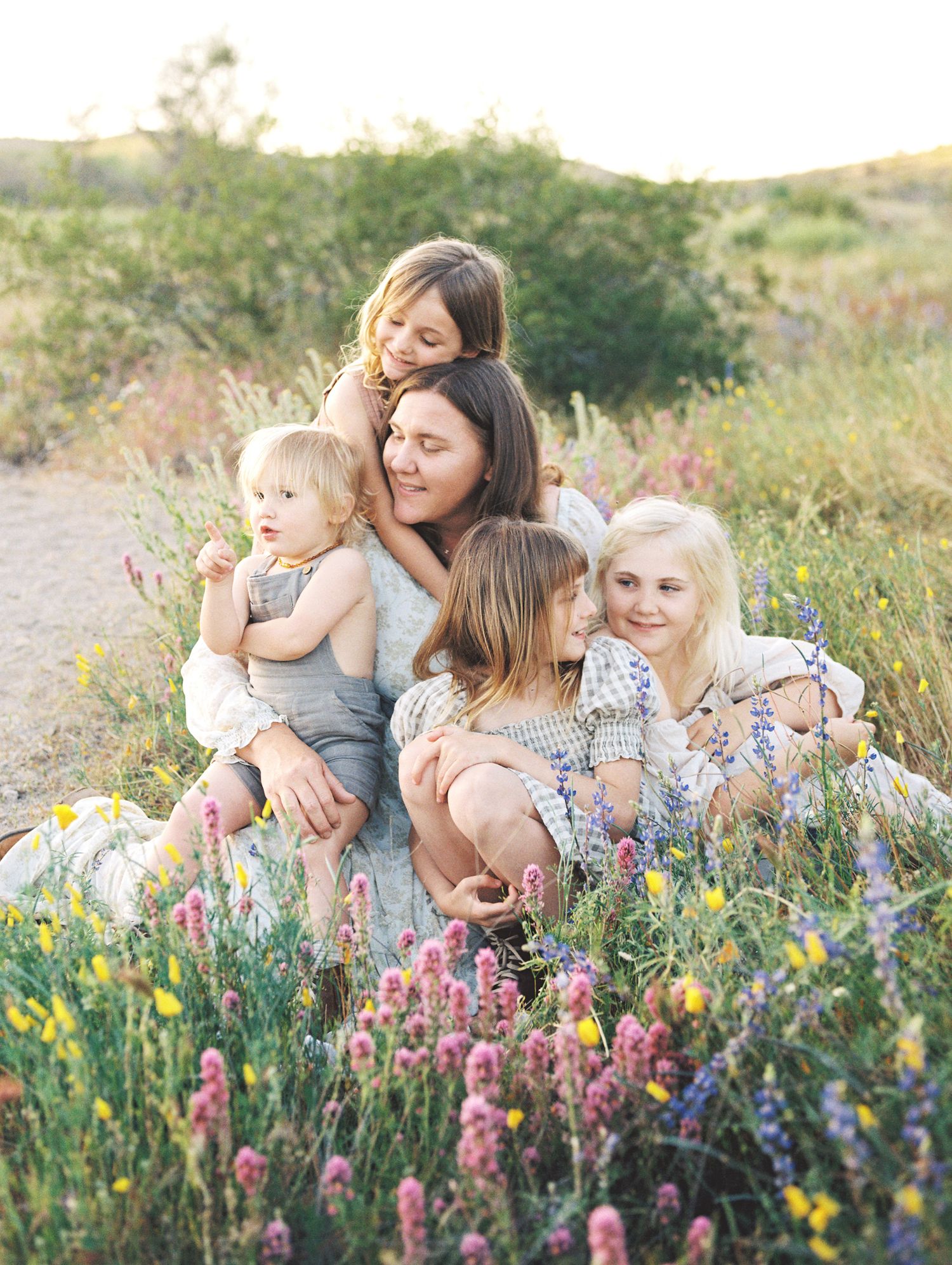 Mother sitting in colorful wildflower field surrounded by four children at sunset.