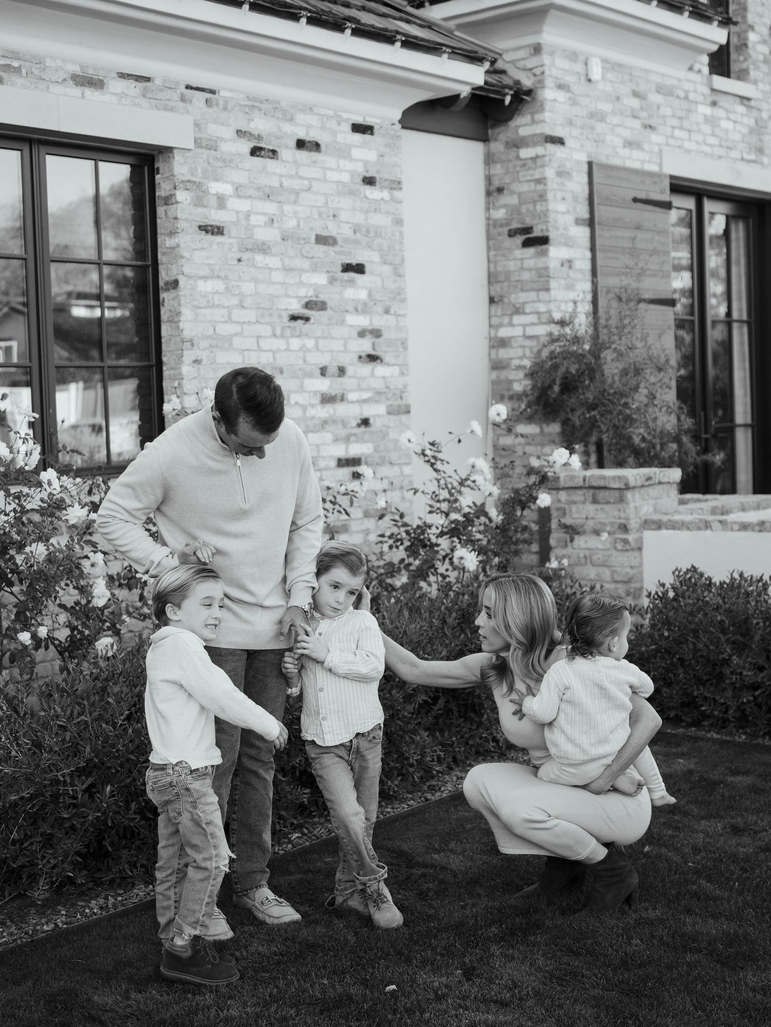 Black and white photo of family of five playing together outside their brick home.