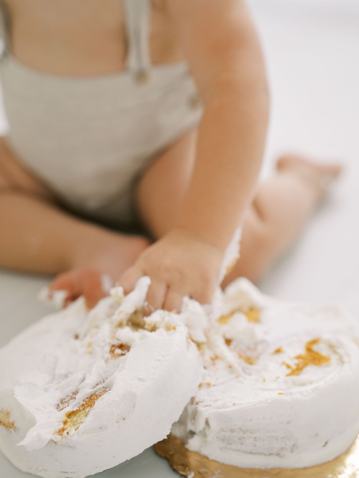 Close-up of baby hands smashing white frosted birthday cake on clean white surface.