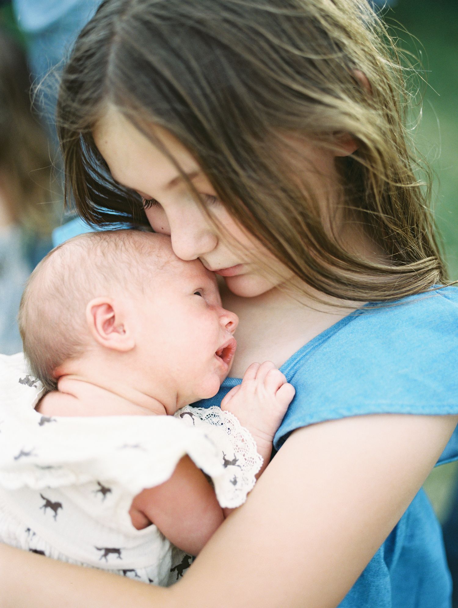 Young girl tenderly holding and nuzzling newborn baby wrapped in white blanket.
