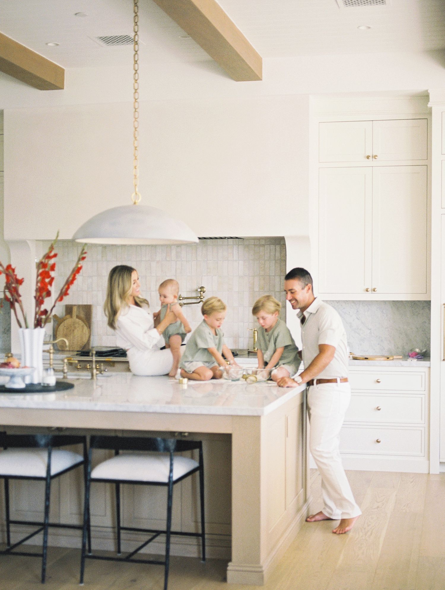 A happy family of five bakes together at a white marble kitchen island in a bright modern home.