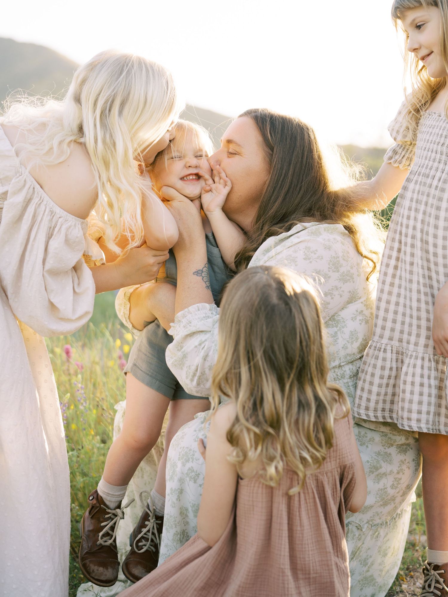 Two women sharing joyful moment with laughing toddler in sunny wildflower meadow.