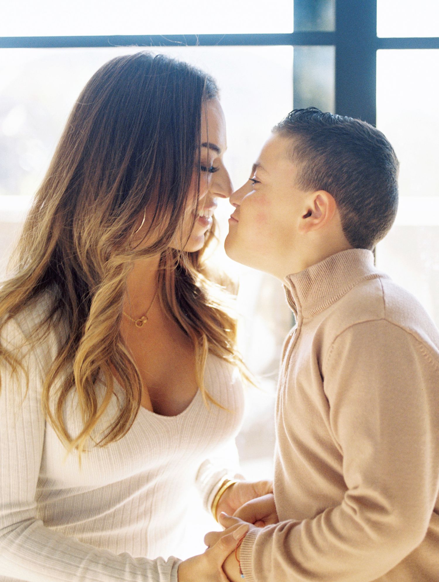 A mother and young son share a tender nose-to-nose moment, smiling warmly in soft natural light.