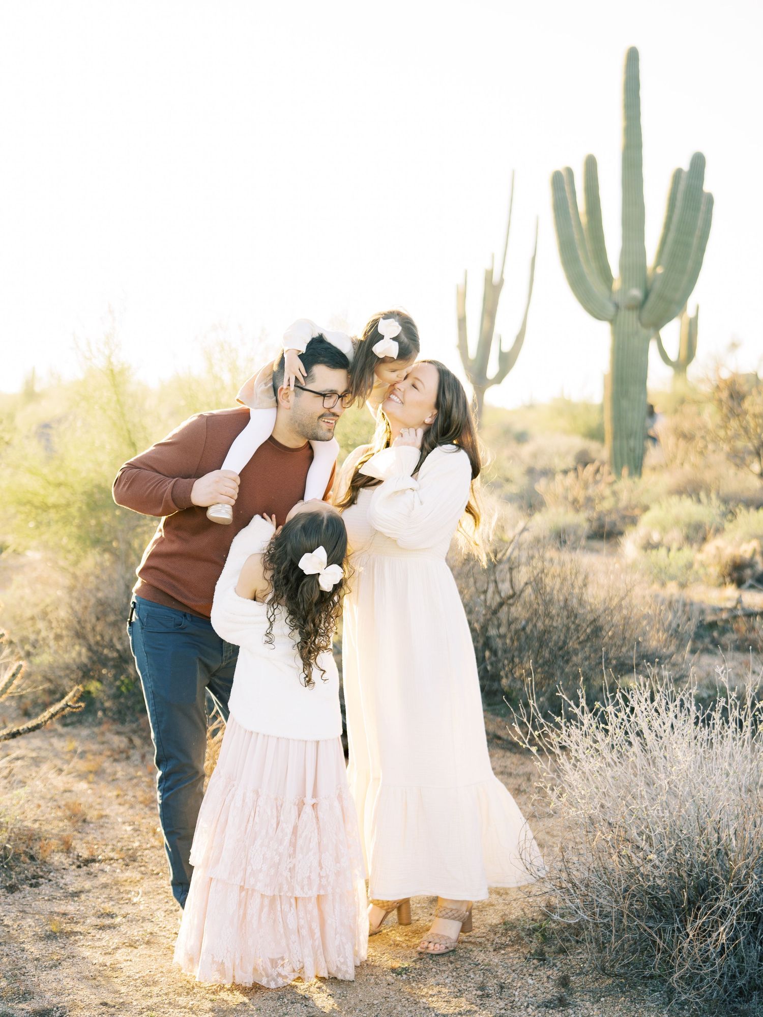 Family of four sharing warm embrace in desert with saguaro cactus backdrop.
