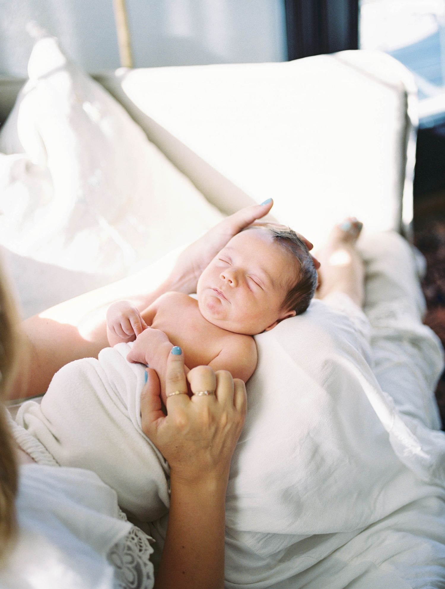 Newborn baby sleeping peacefully wrapped in white blanket in soft sunlight.