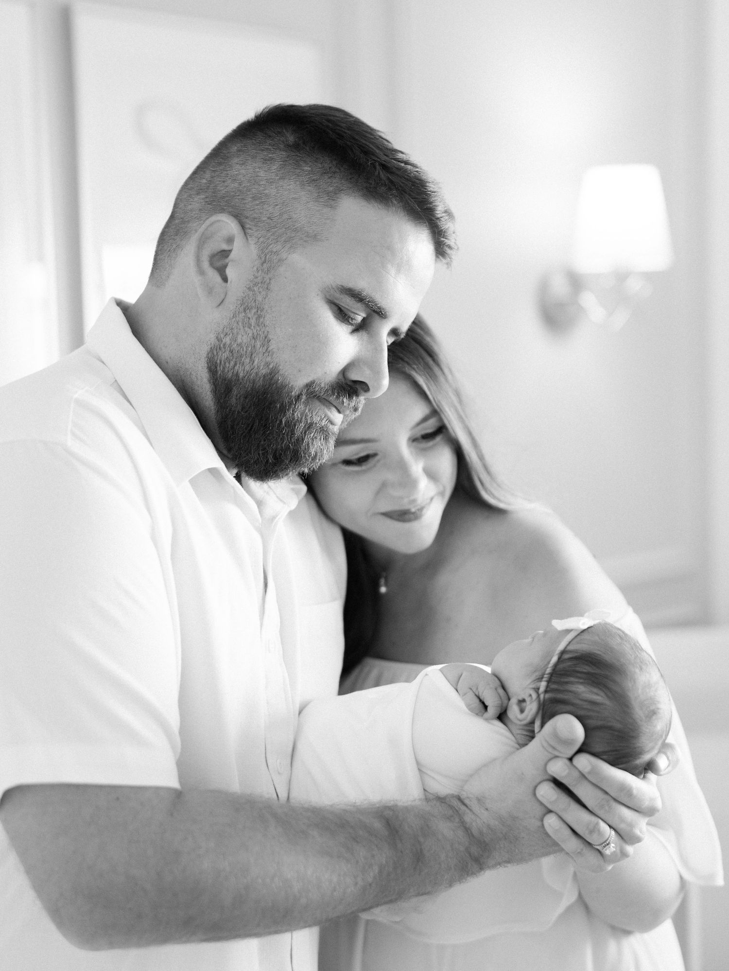 Black and white portrait of couple tenderly holding sleeping newborn baby together.
