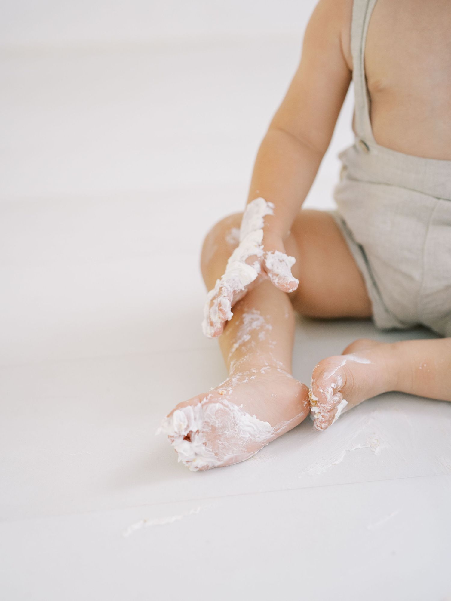 Baby's feet and legs covered in cake frosting during a first birthday cake smash photo session.