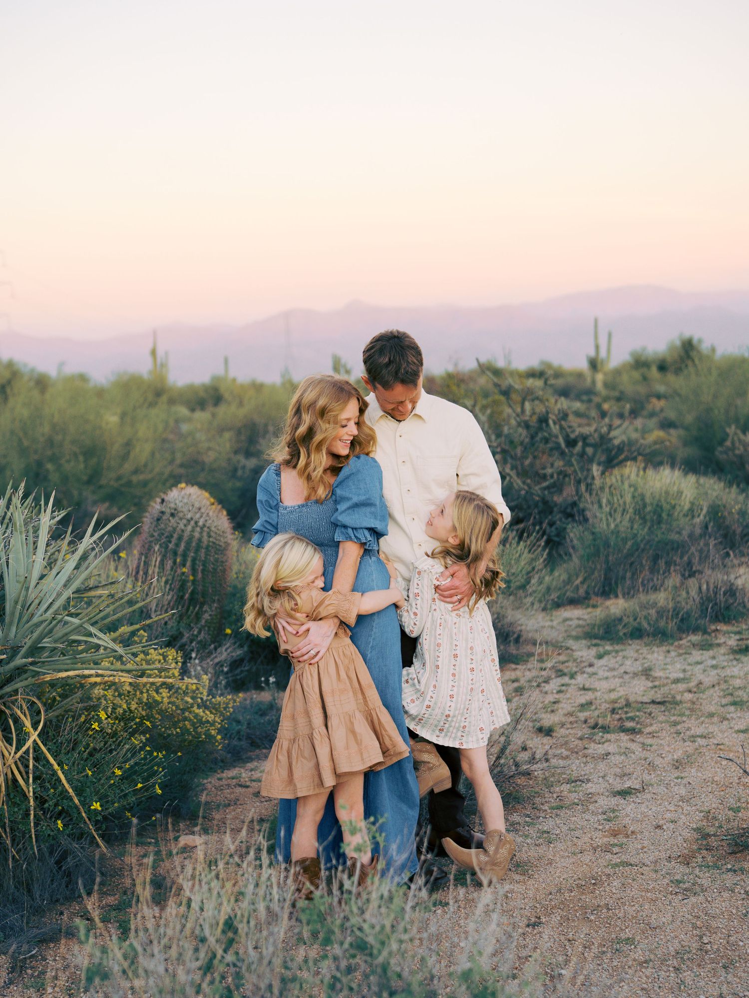Family of four embracing in Arizona desert at dusk with mountain backdrop.
