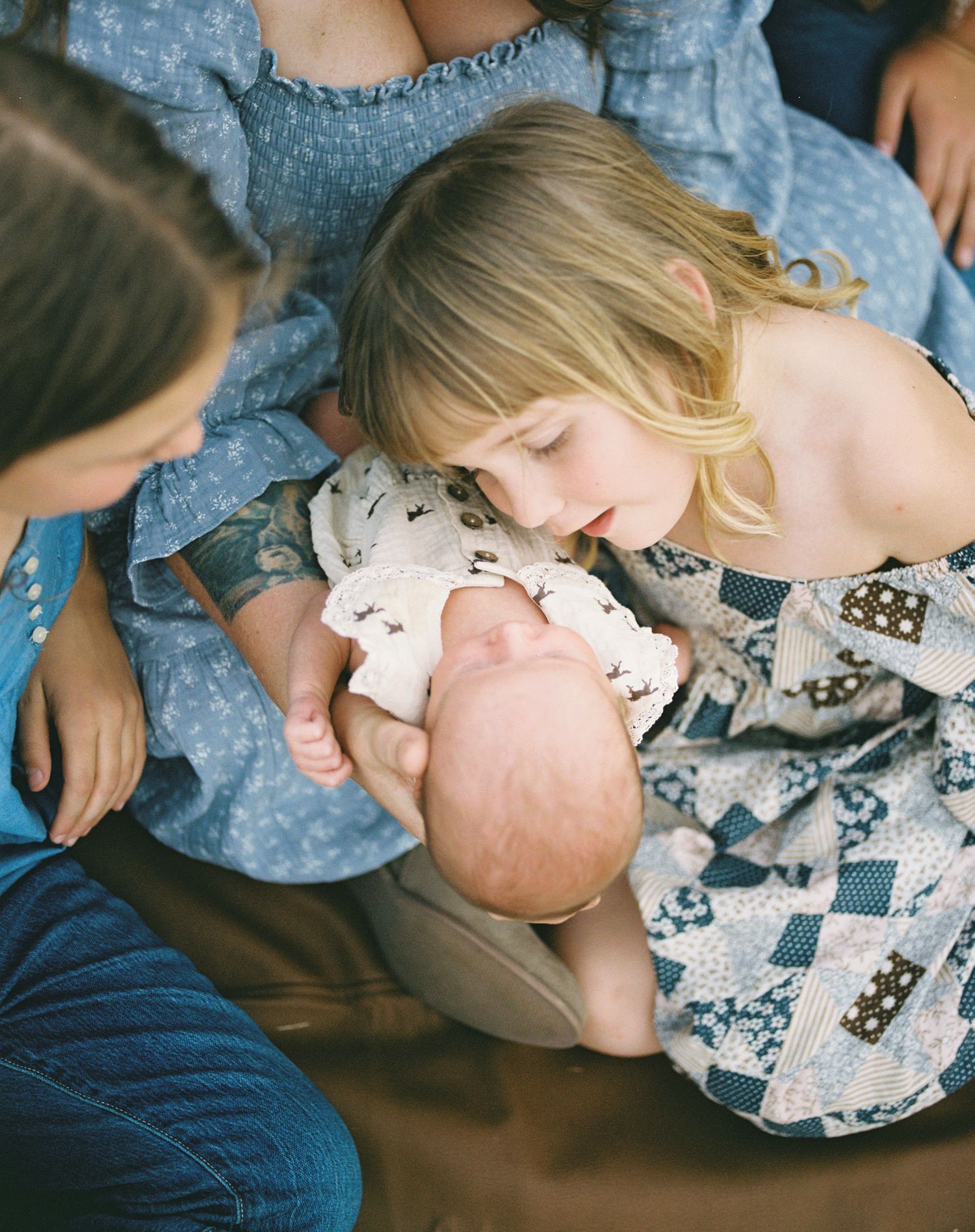 Young girl tenderly kissing newborn sibling held by mother during family newborn session.