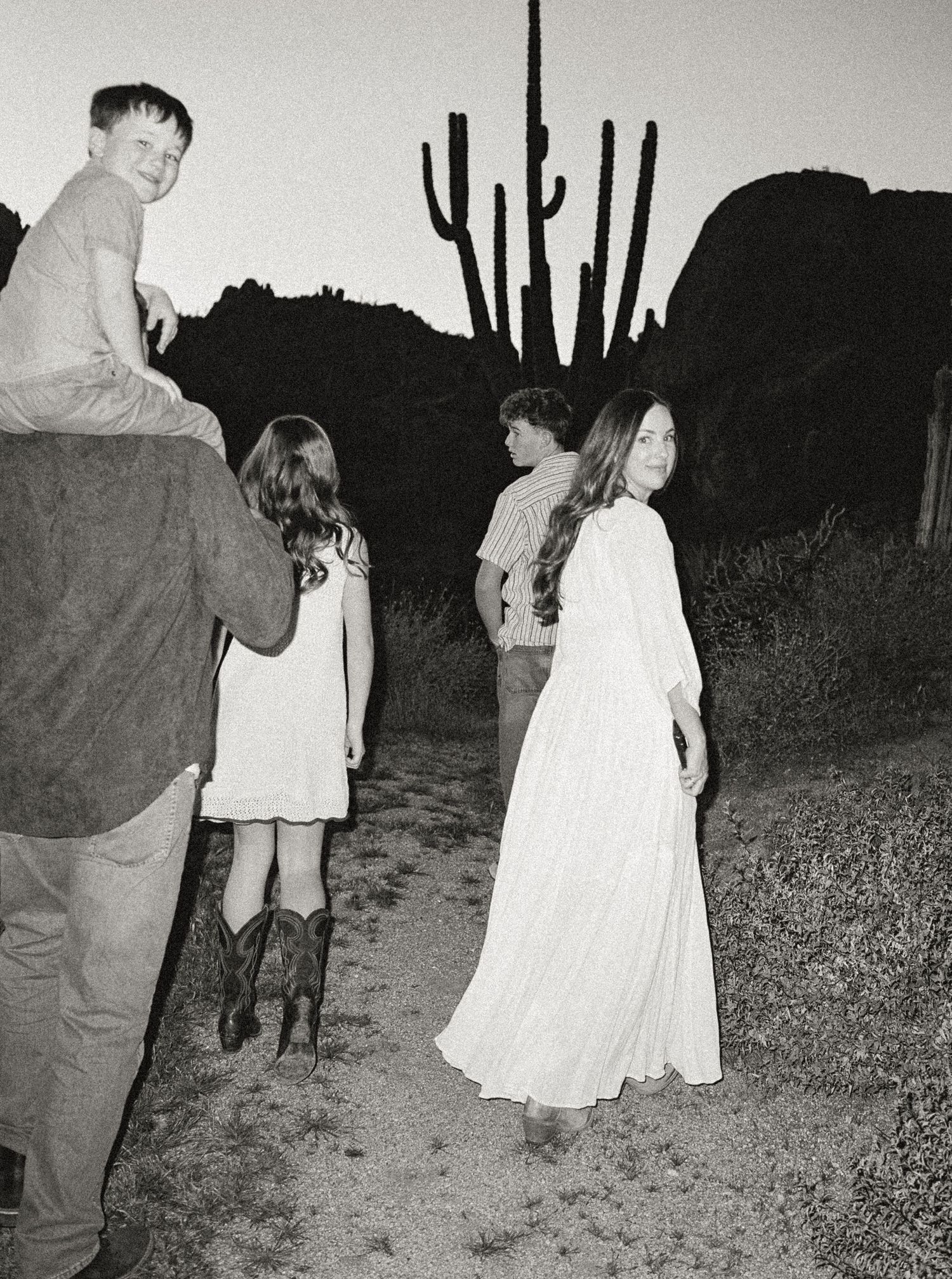 Black and white film photo of family walking at dusk with saguaro cactus silhouette in background.