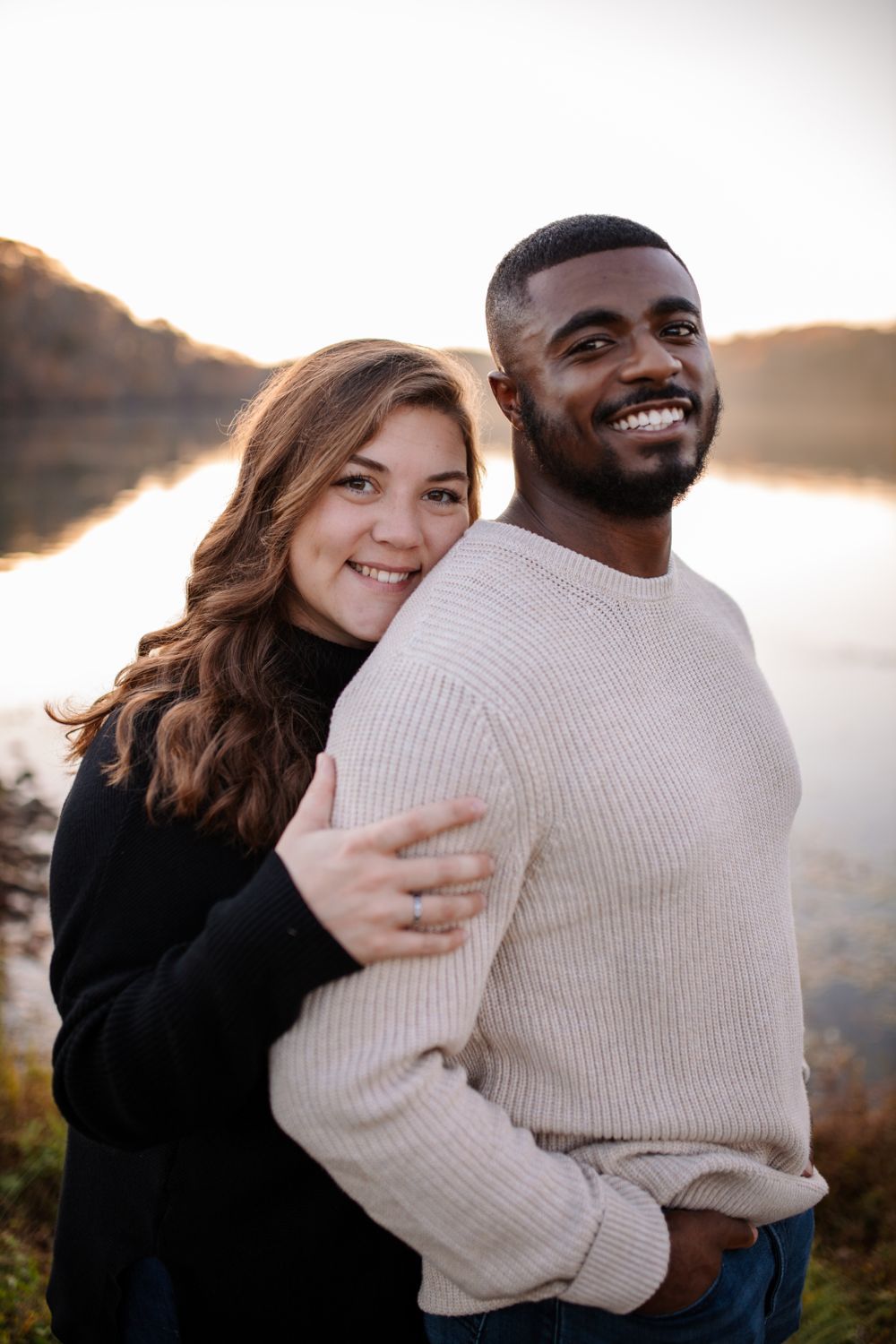 Couple embracing and smiling by a lake at golden hour
