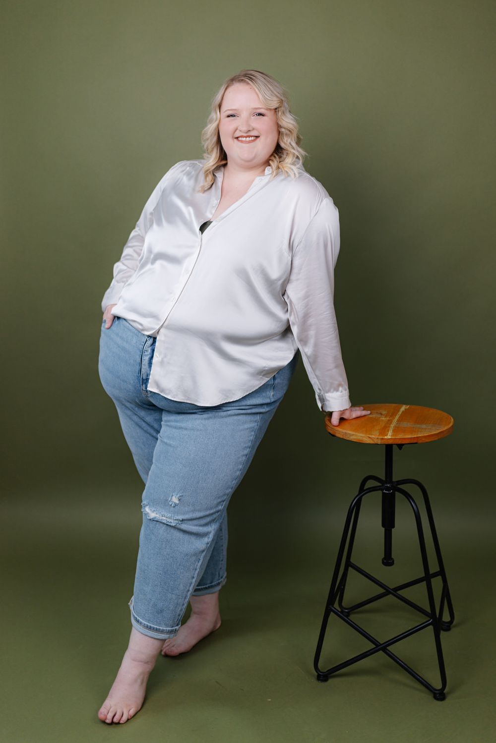 Charli leaning on a wooden stool against an olive backdrop