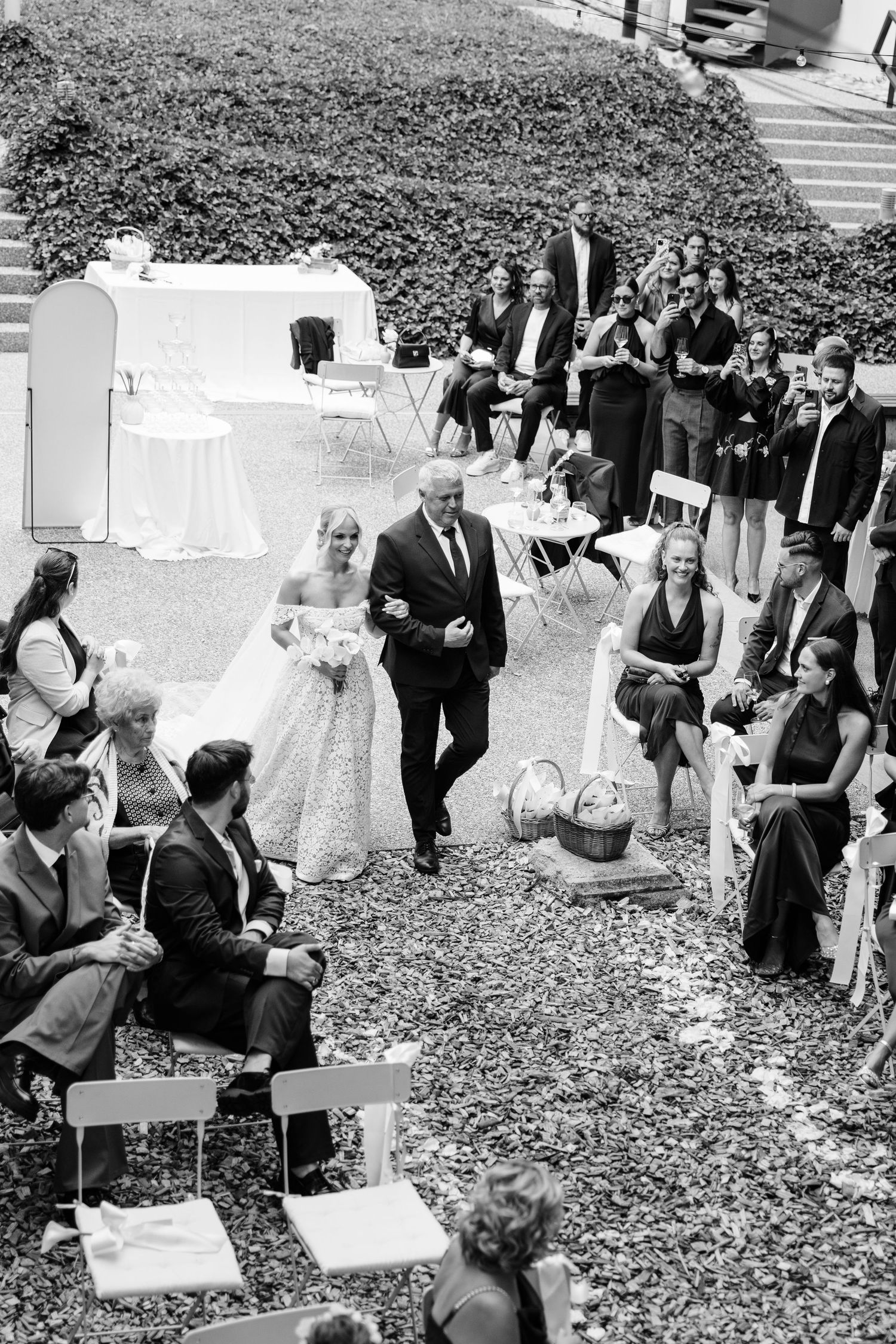 Aerial black and white photo of bride walking down outdoor wedding aisle with her father.