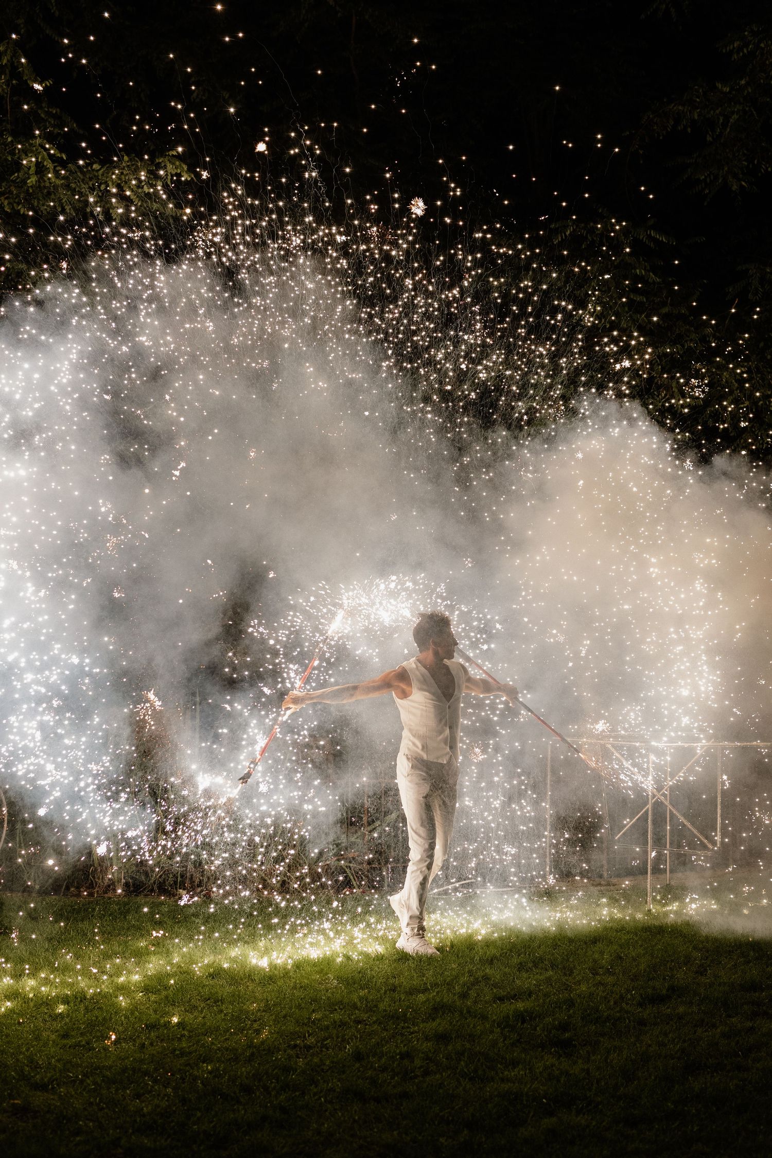 Person standing amid spectacular white sparkler fireworks display at night outdoors.