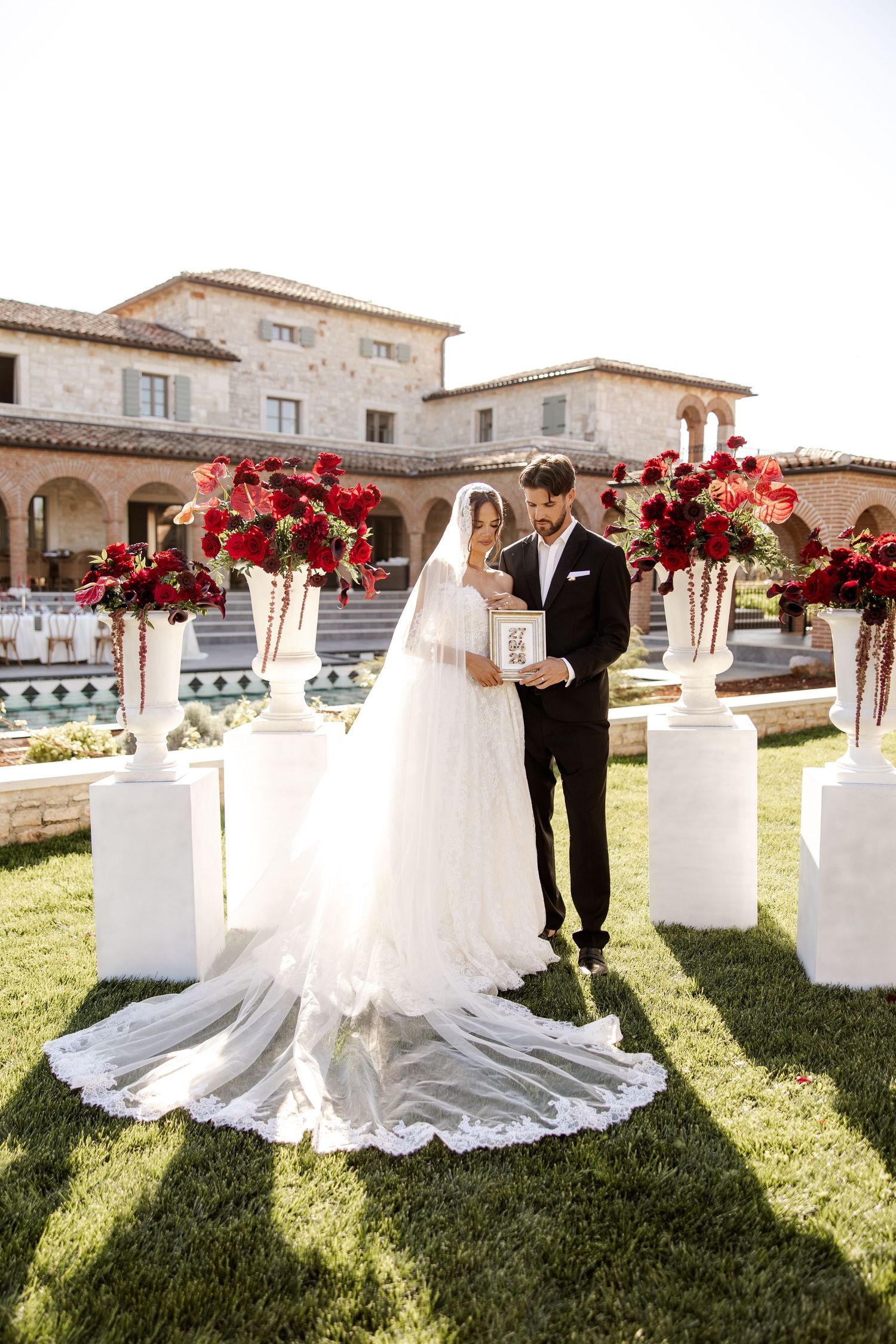 Bride and groom exchanging vows outdoors surrounded by red floral arrangements.
