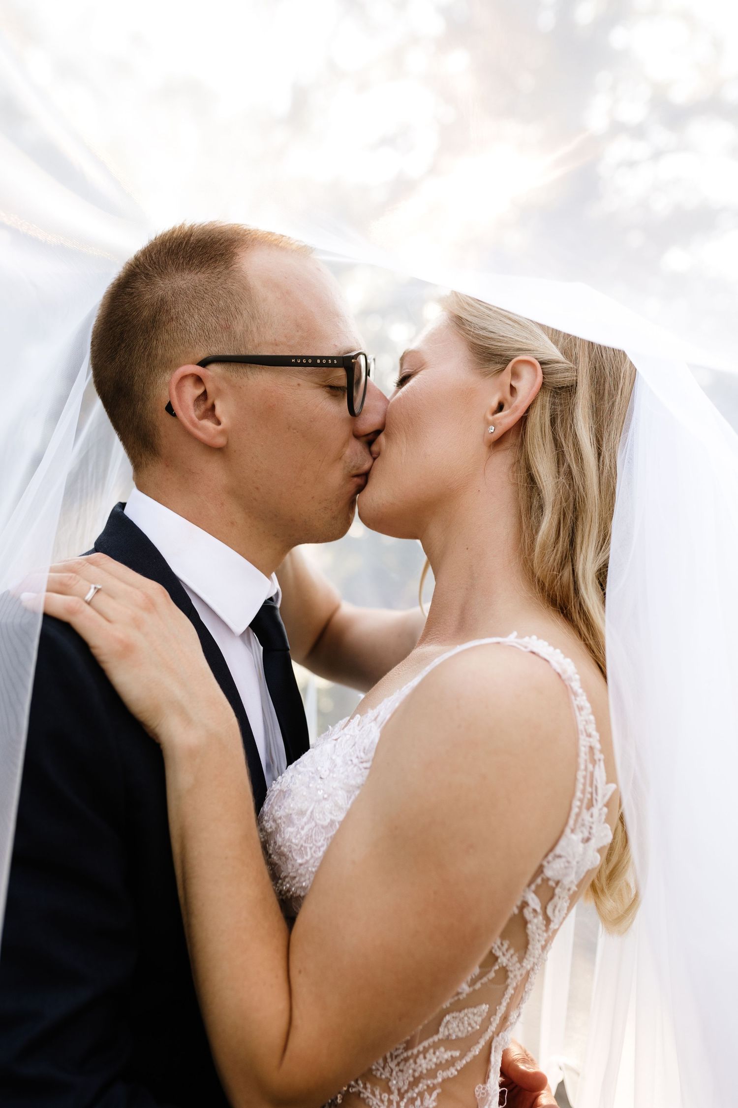 Bride and groom sharing a romantic kiss under a flowing white veil on their wedding day.