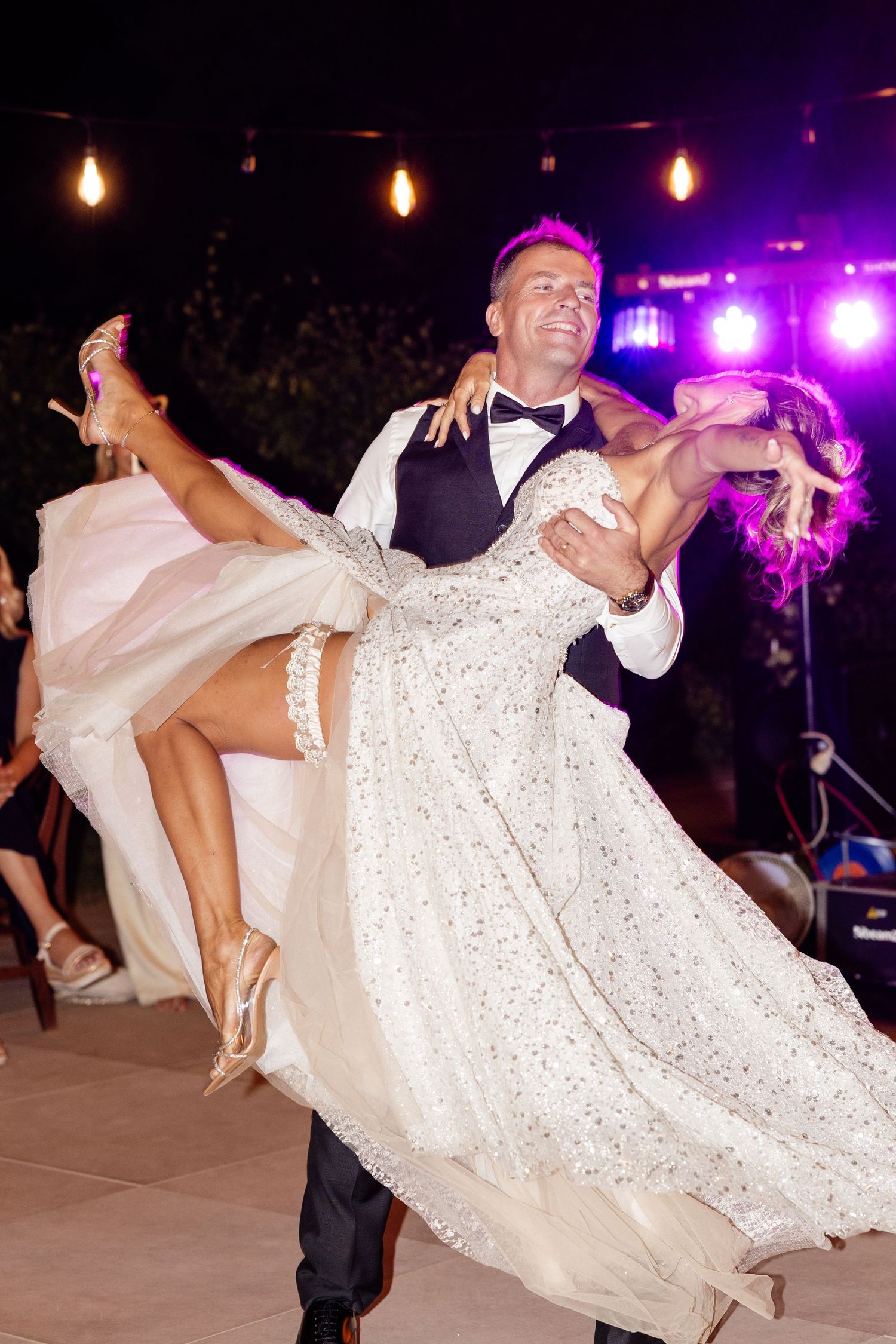 Groom lifts bride in elegant white gown during romantic first dance at wedding reception.