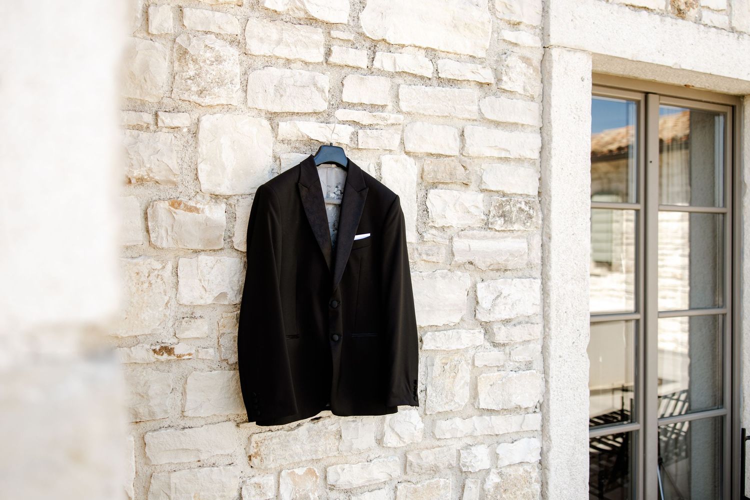 Black suit jacket hanging on a hanger against a rustic white stone wall outdoors.