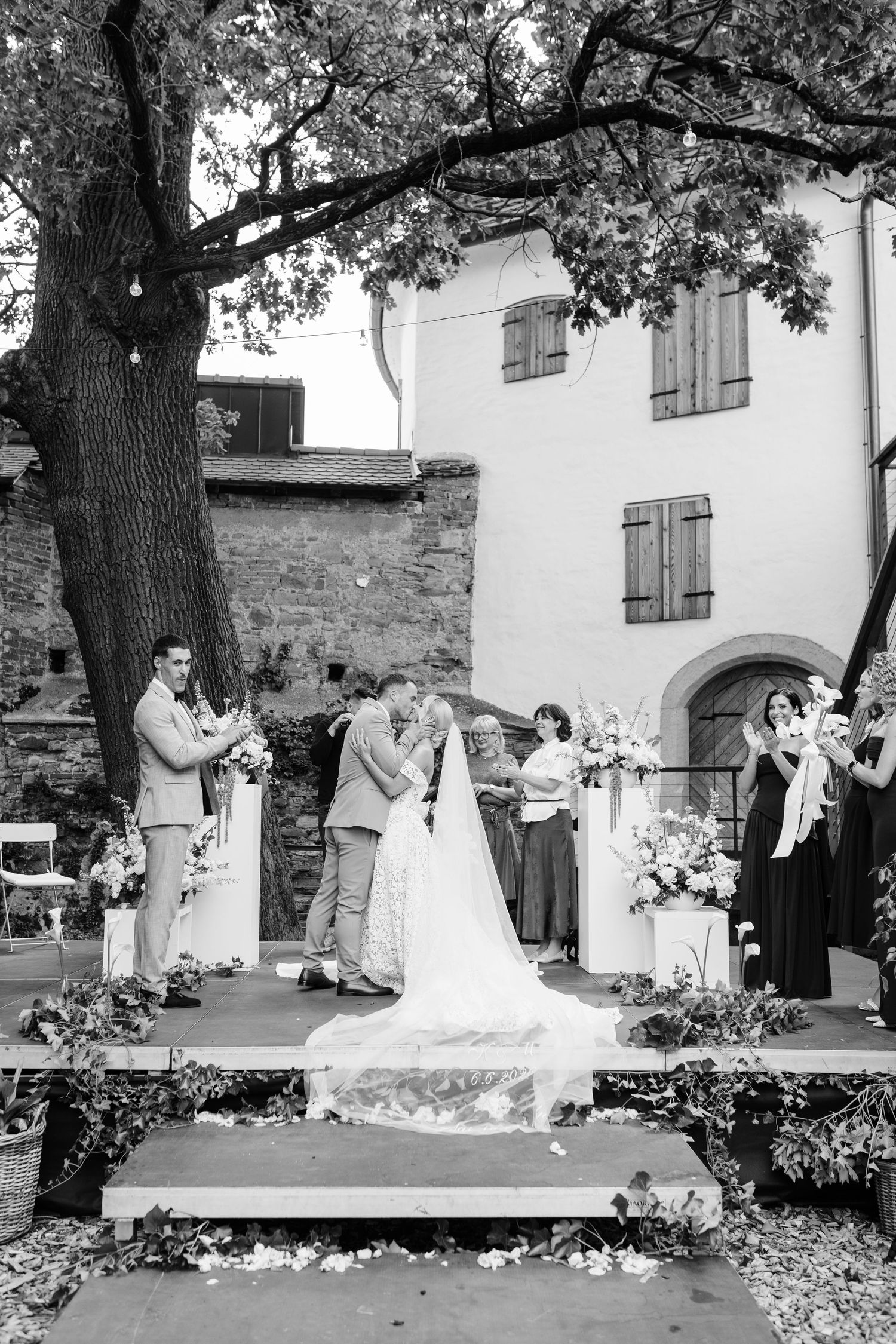 Bride and groom share first kiss on outdoor wedding altar surrounded by floral arrangements and guests.