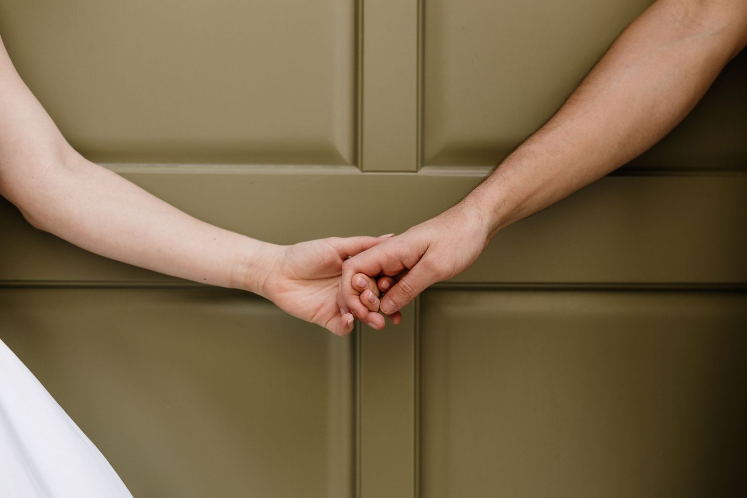 Two people gently holding hands against an olive green paneled wall, symbolizing love and connection.