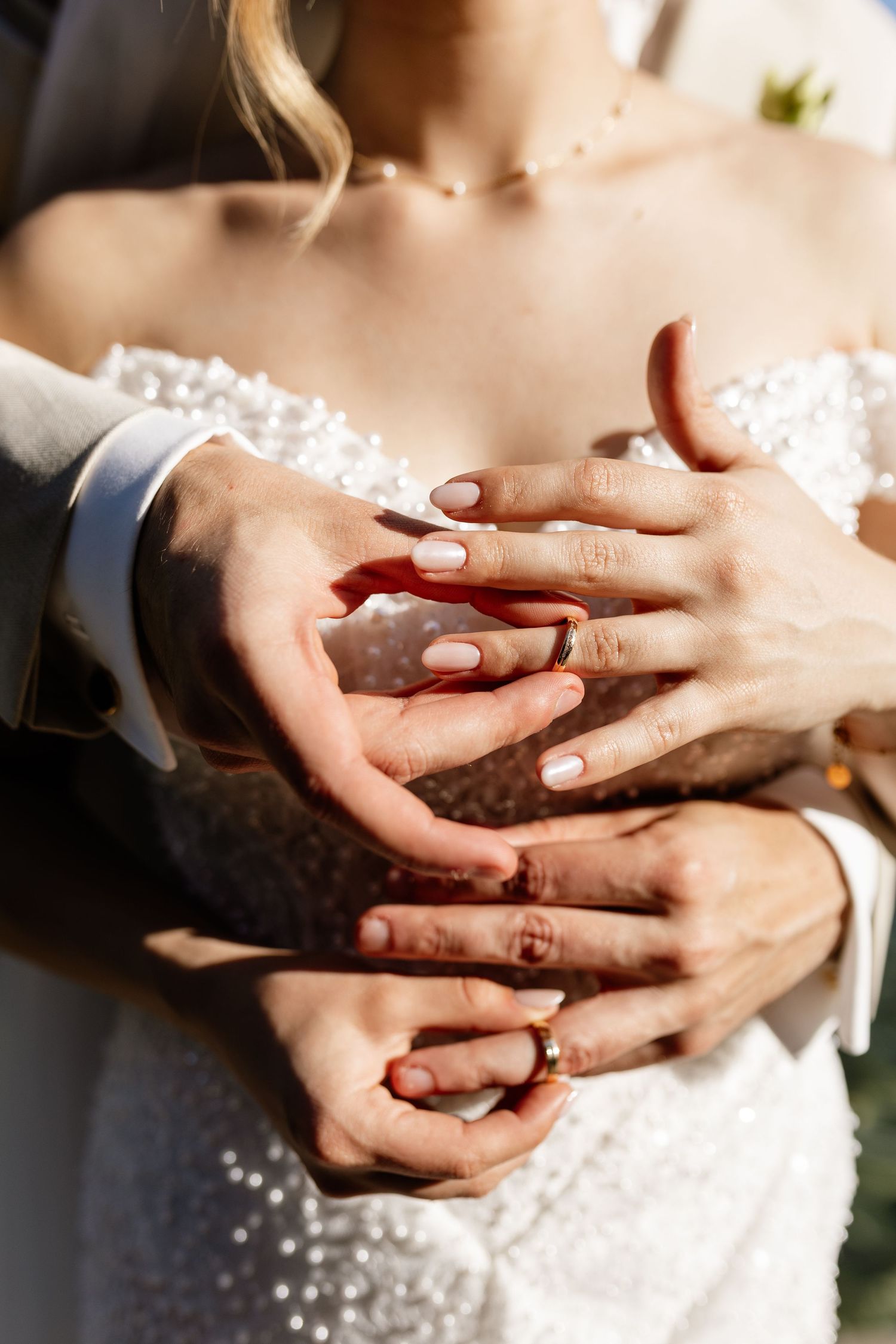 Bride and groom intertwining hands showing wedding rings, close-up shot of couple holding hands in wedding attire.