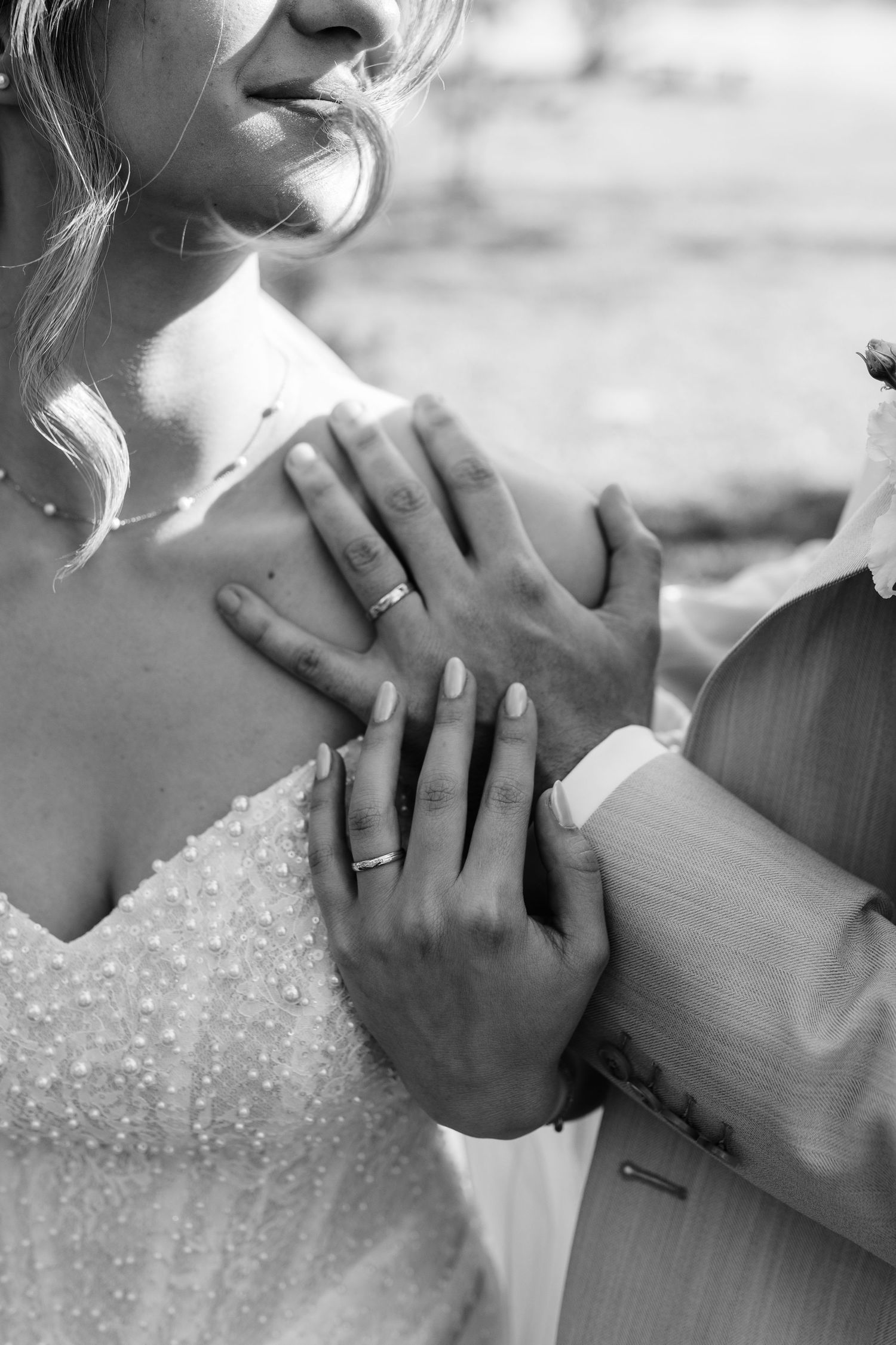 Black and white close-up of bride and groom hands showing wedding rings on brides lace dress.