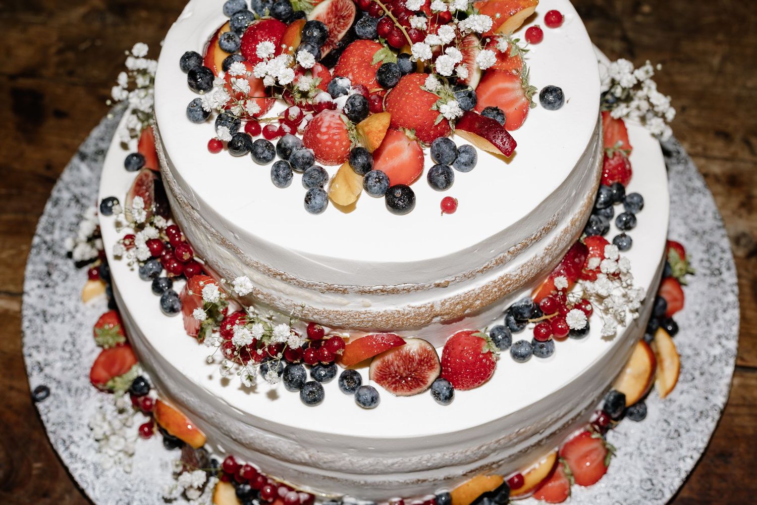 Two-tier naked wedding cake topped with fresh strawberries, blueberries, and mixed berries with white floral accents.