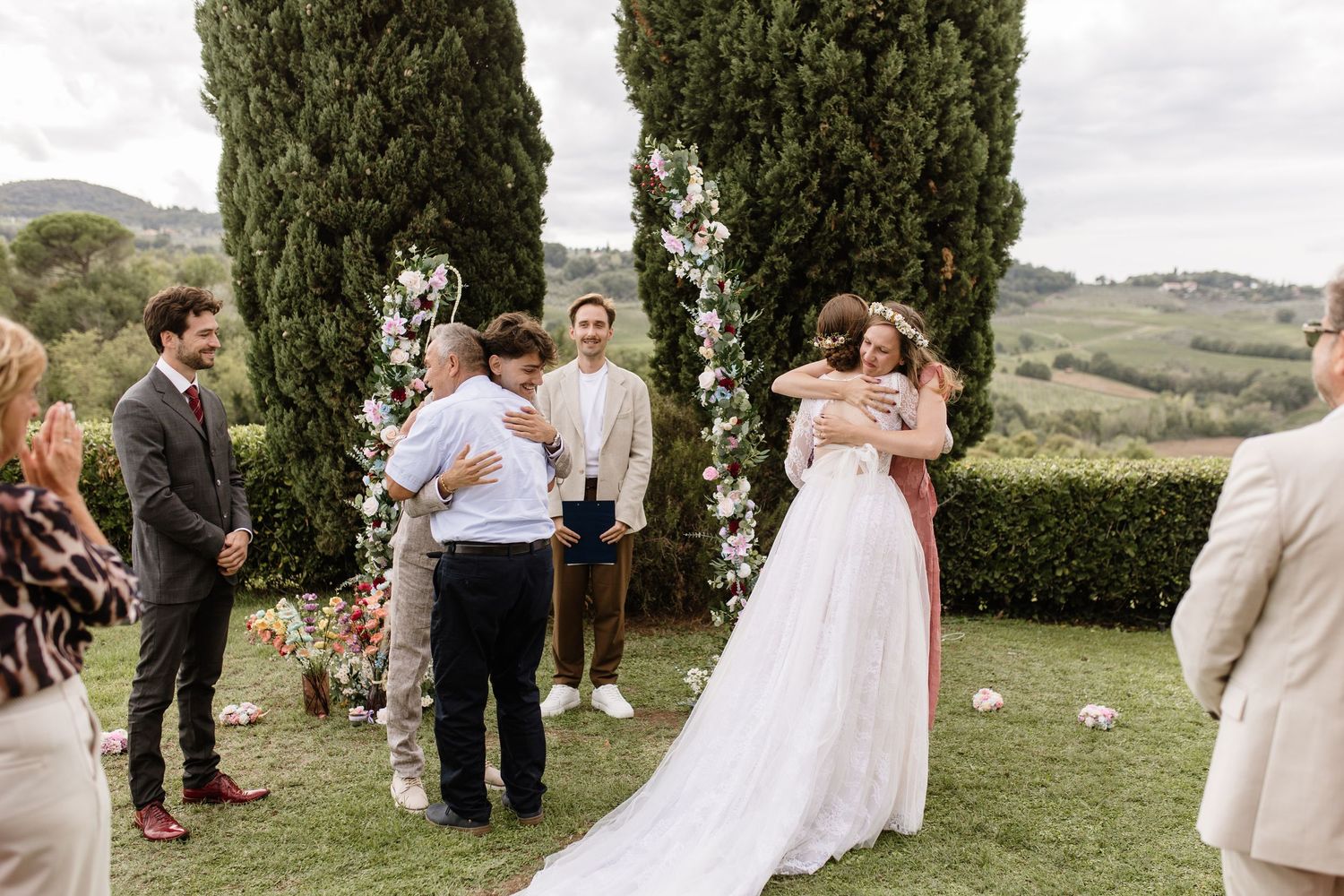 Bride and groom share hugs with guests at an outdoor wedding ceremony in a scenic Tuscan countryside setting.