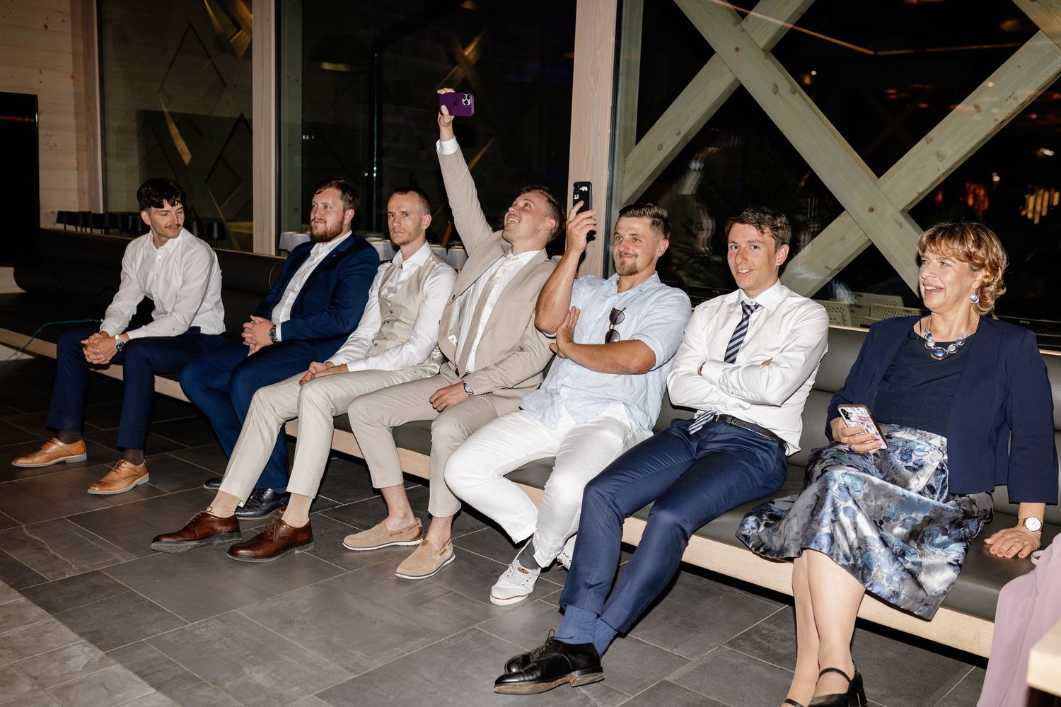 Group of people sitting on benches at an indoor event, one raising their hand.
