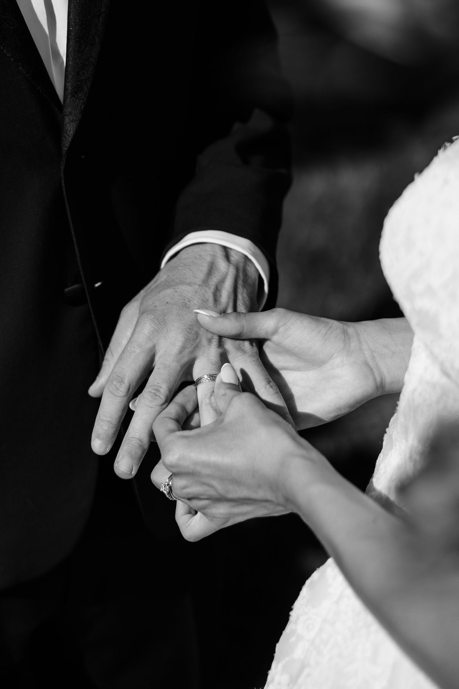 Black and white close-up of bride placing wedding ring on grooms finger during the ring exchange ceremony.