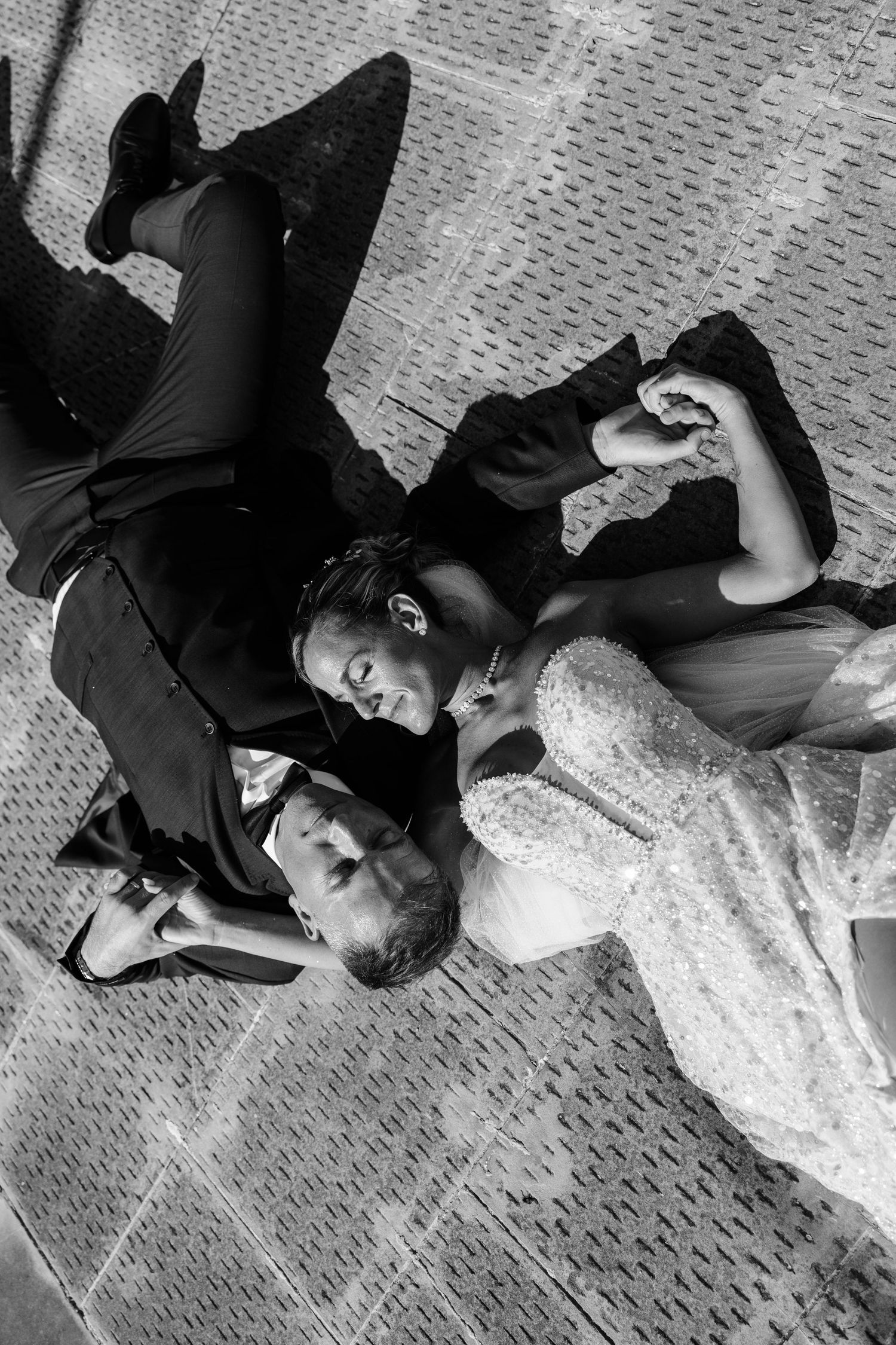 Black and white aerial shot of bride and groom lying on a decorative tiled floor together.