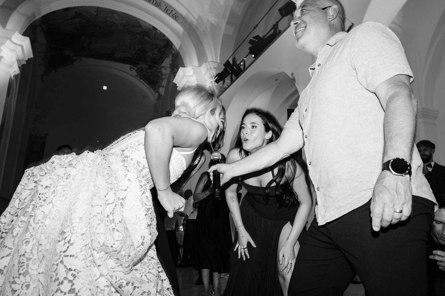 Black and white photo of wedding guests dancing energetically at lively reception party celebration.
