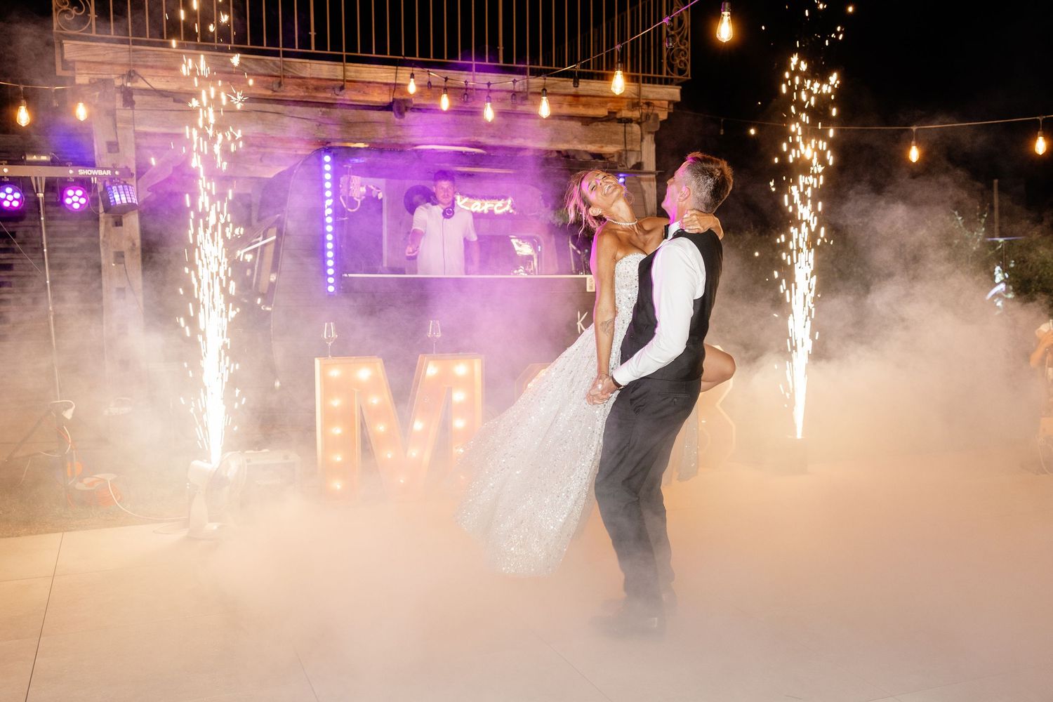 Bride and groom share first dance surrounded by sparkling fireworks and fog on a romantic wedding dance floor.