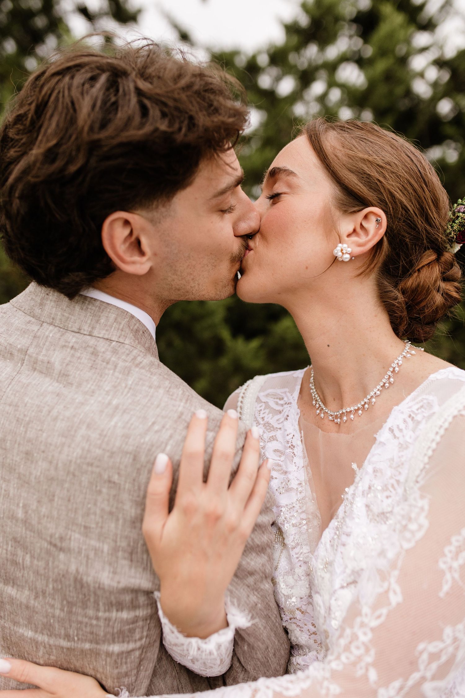 Bride and groom share first kiss surrounded by green trees after outdoor wedding ceremony.