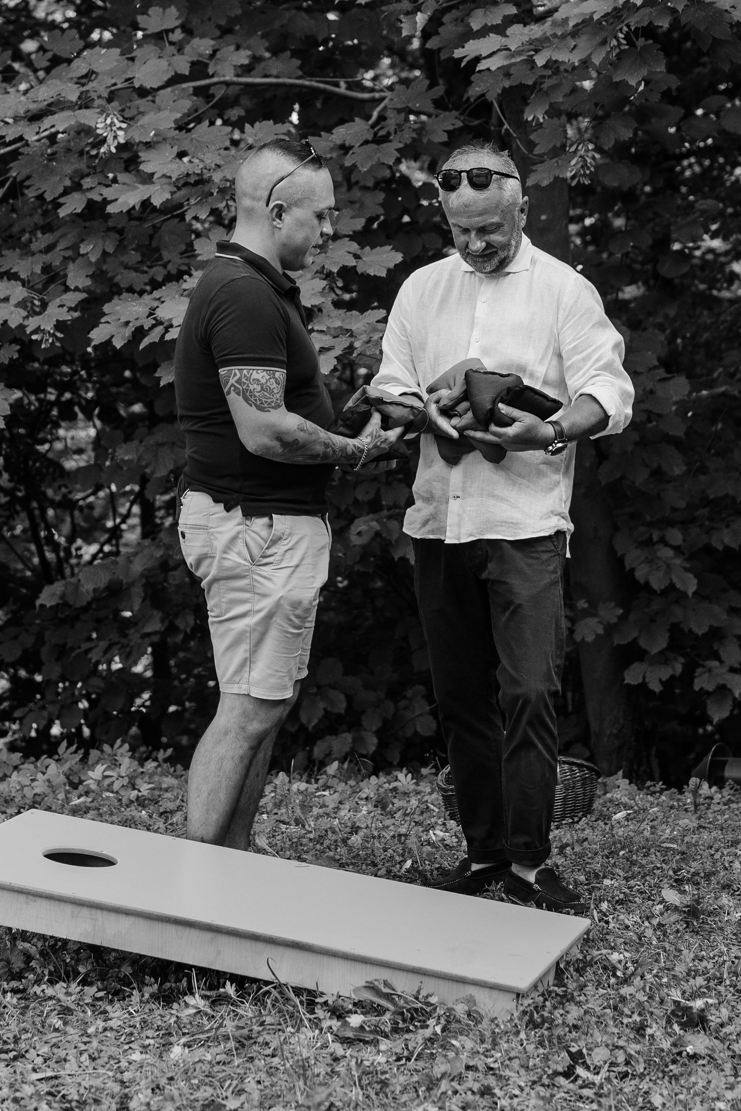 Two men in casual attire playing cornhole lawn game outdoors in black and white photo.