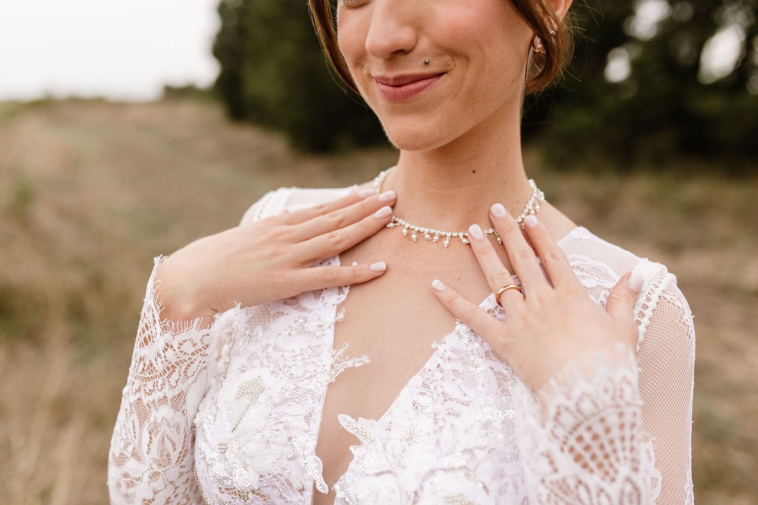 Close-up of bride in lace wedding dress showcasing elegant pearl necklace and diamond ring jewelry details.