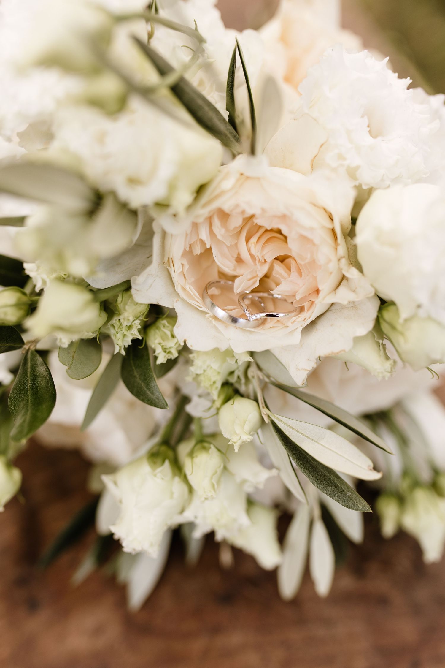 Elegant wedding bouquet with cream roses and white flowers, featuring two gold wedding rings nestled among greenery.