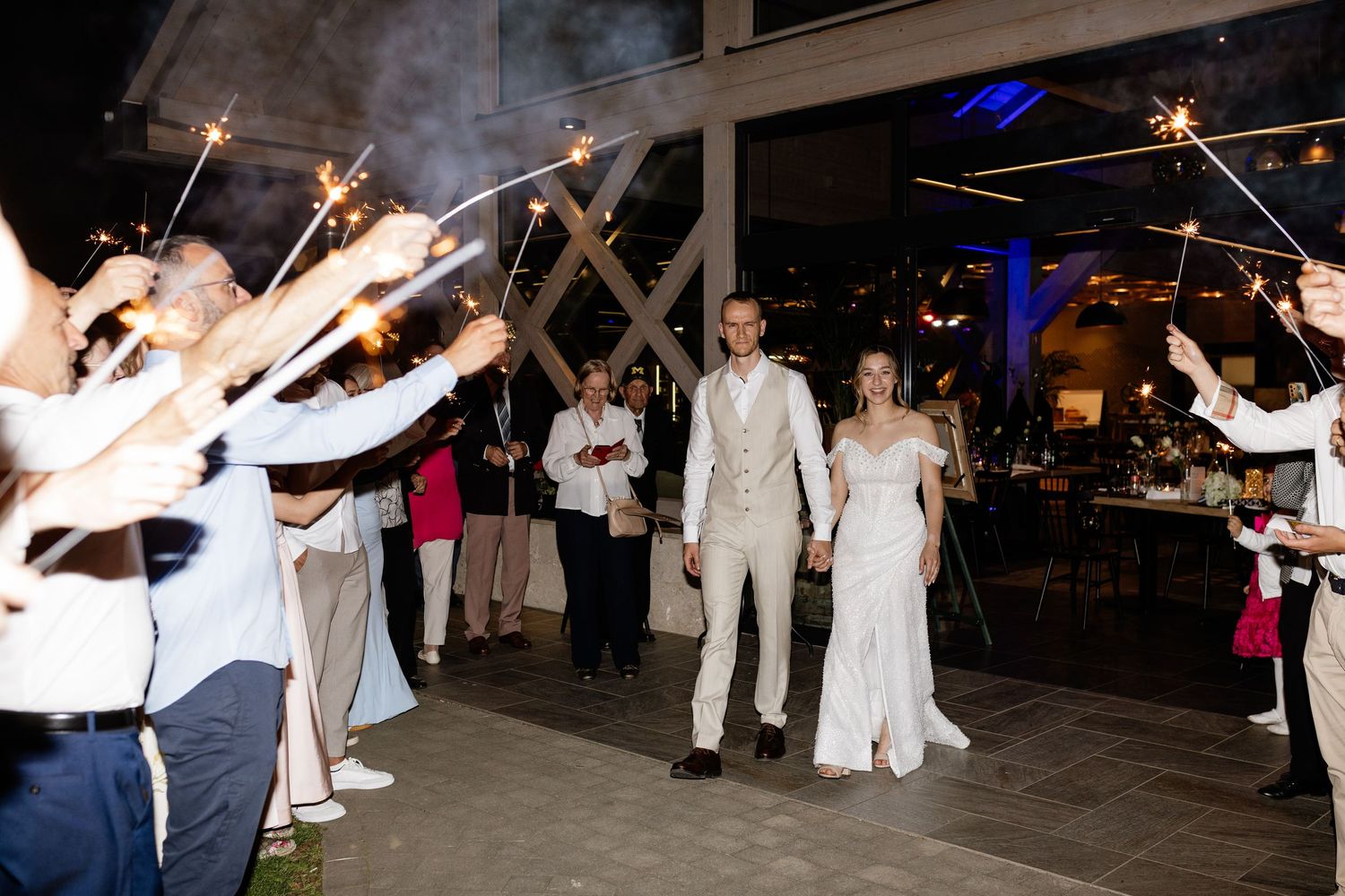 Newlywed couple exits their wedding reception through a sparkler tunnel surrounded by cheering guests.