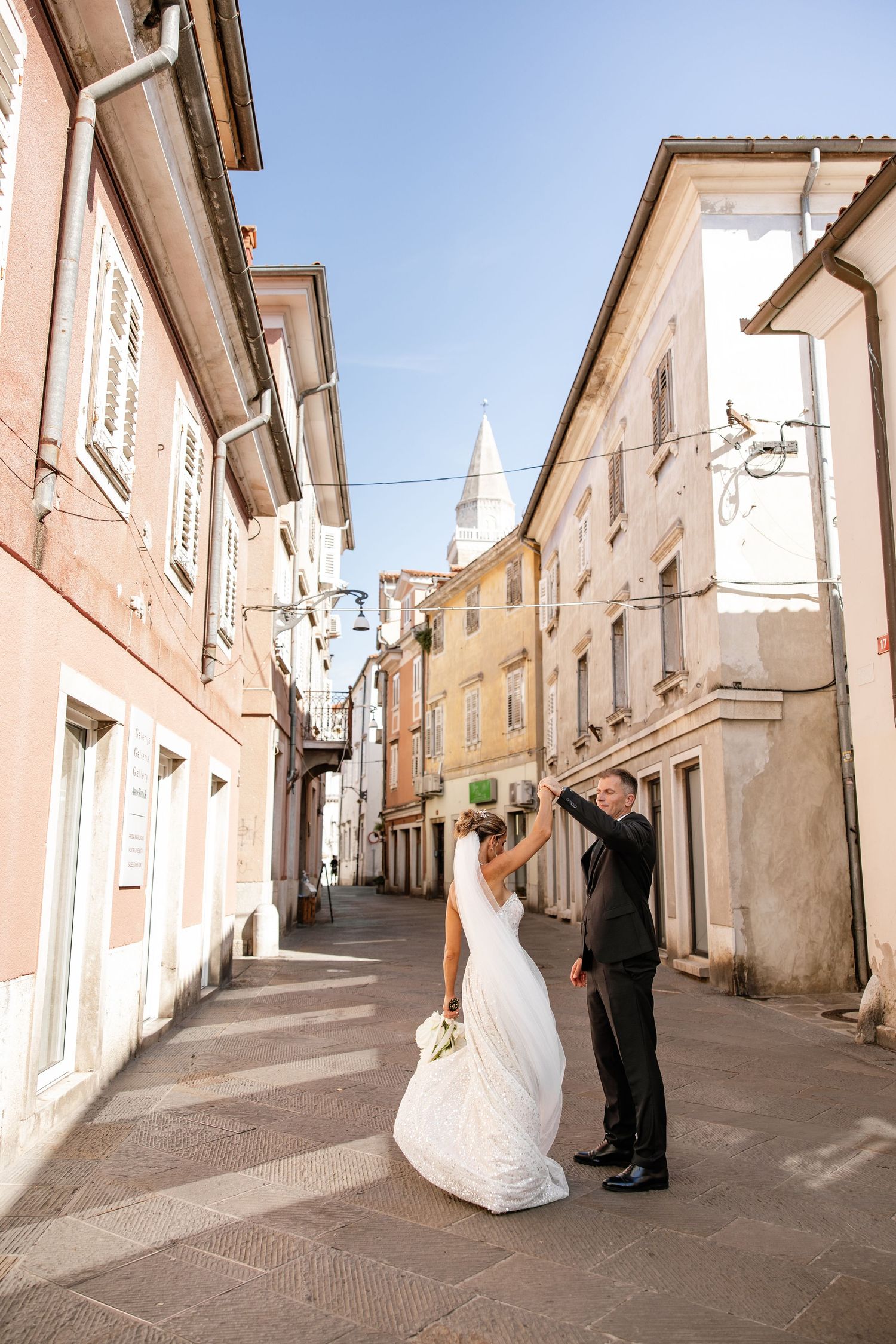 Bride and groom dance joyfully in a charming European cobblestone street with historic buildings.
