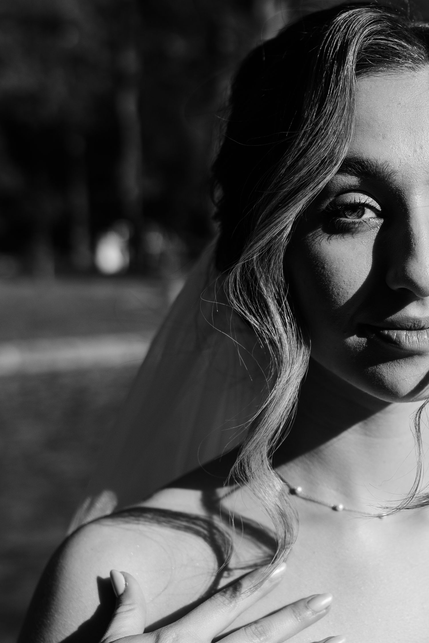 Black and white bridal portrait of a blonde woman wearing a veil and pearl necklace in soft dramatic lighting.