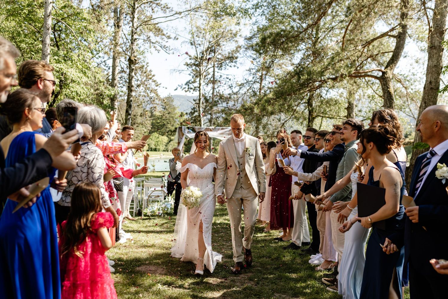 Newlyweds walk joyfully through cheering guests lining the aisle at an outdoor wedding ceremony.