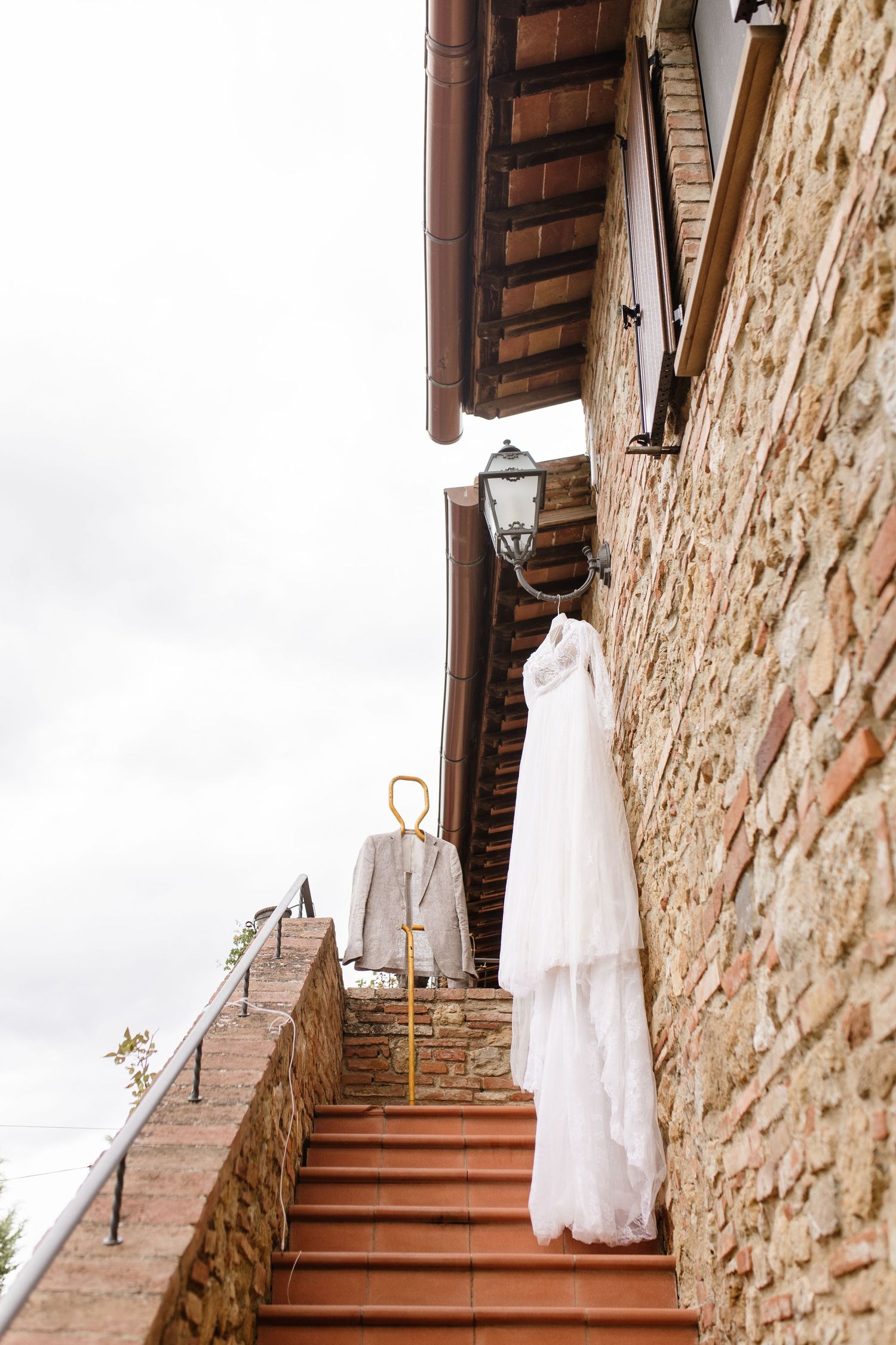 Wedding dress and suit hanging on a rustic stone building staircase in Tuscany, Italy.
