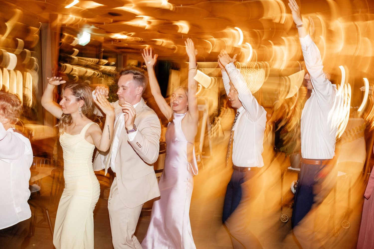 Joyful wedding guests dancing energetically at a warmly lit indoor wedding reception celebration.