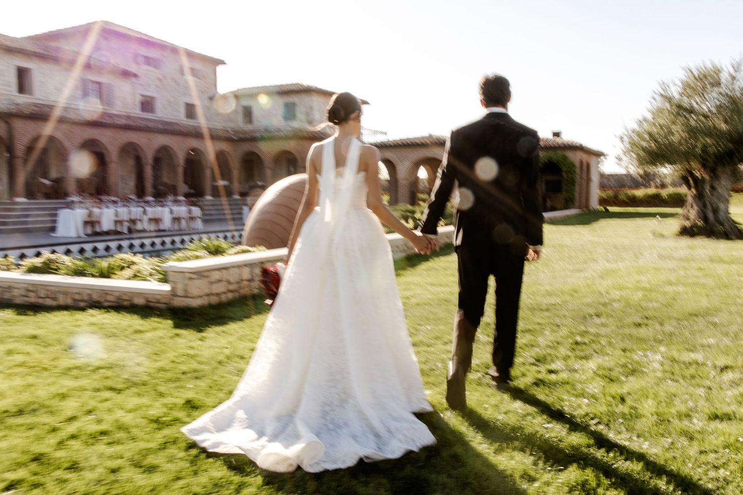 Bride and groom walking hand in hand on lush green lawn at elegant outdoor wedding venue.