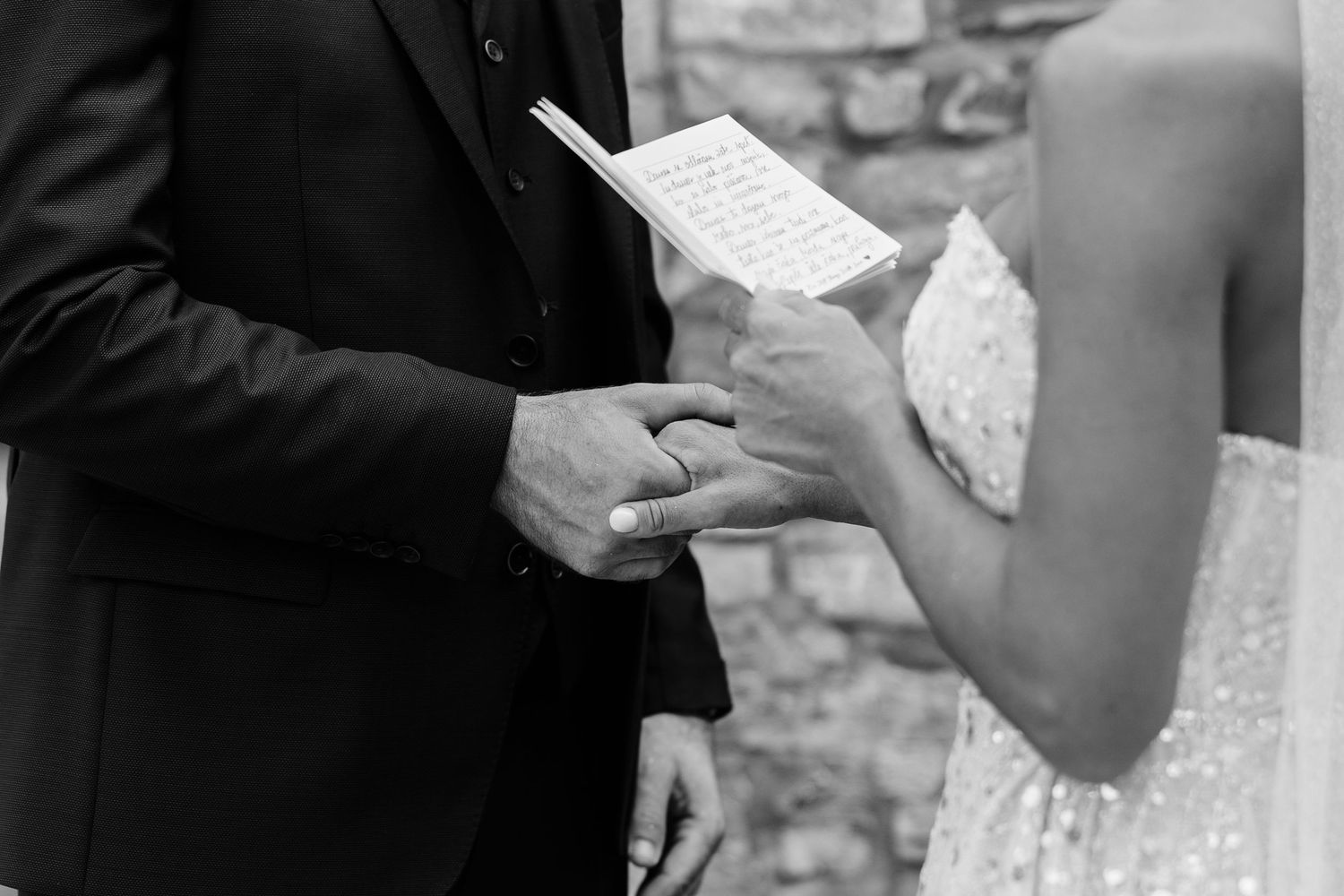 Black and white photo of bride and groom exchanging rings during outdoor wedding ceremony.