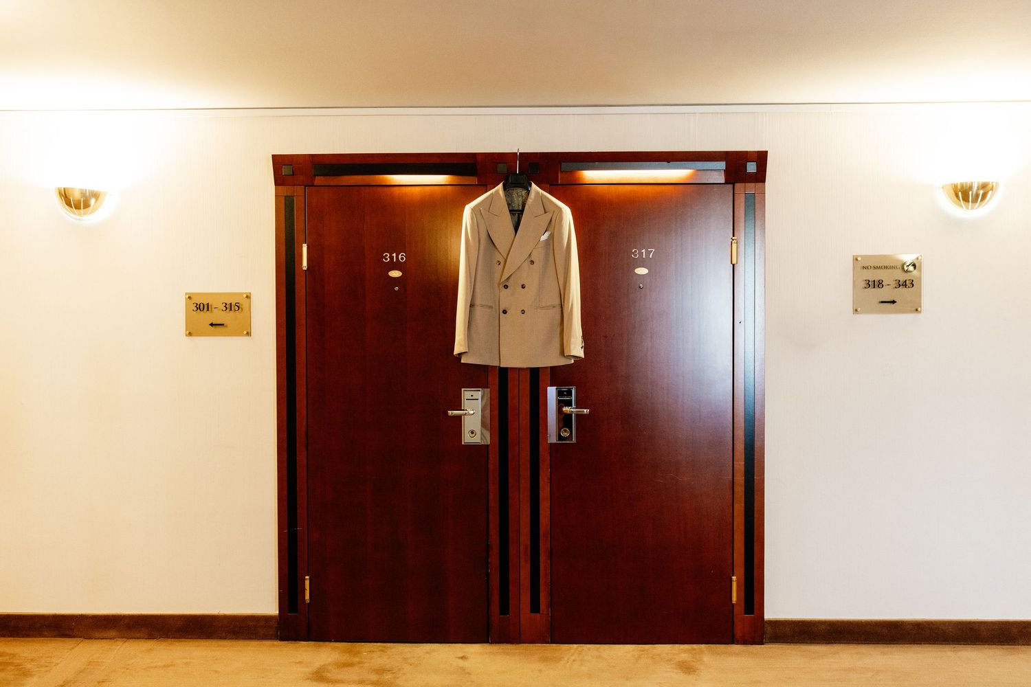 Elegant light gray double-breasted suit jacket hanging on ornate wooden hotel room doors.